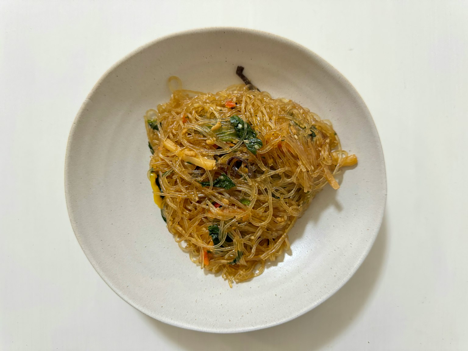 Hidangan mi kaca tumis dengan sayuran di atas piring putih