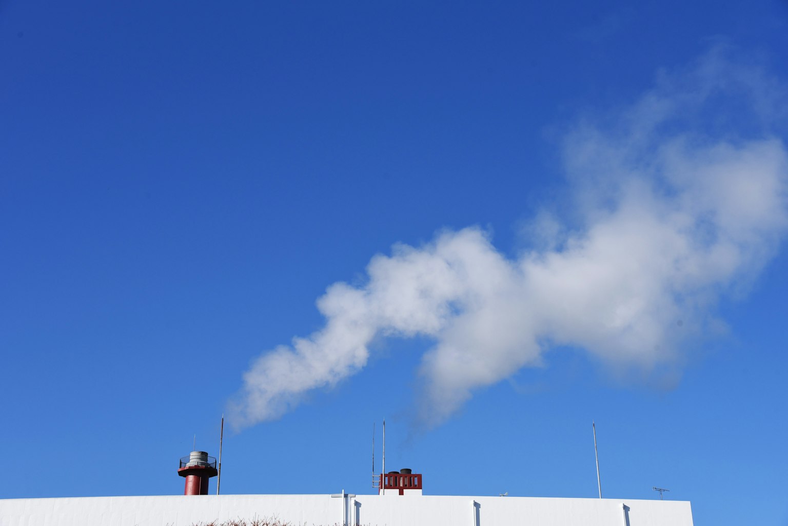 Caminetto che emette fumo contro un cielo blu chiaro con un edificio bianco