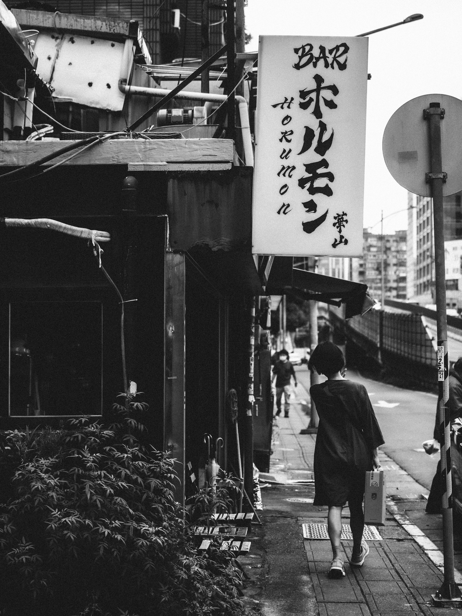 Una persona caminando por una calle con un letrero en un ambiente en blanco y negro