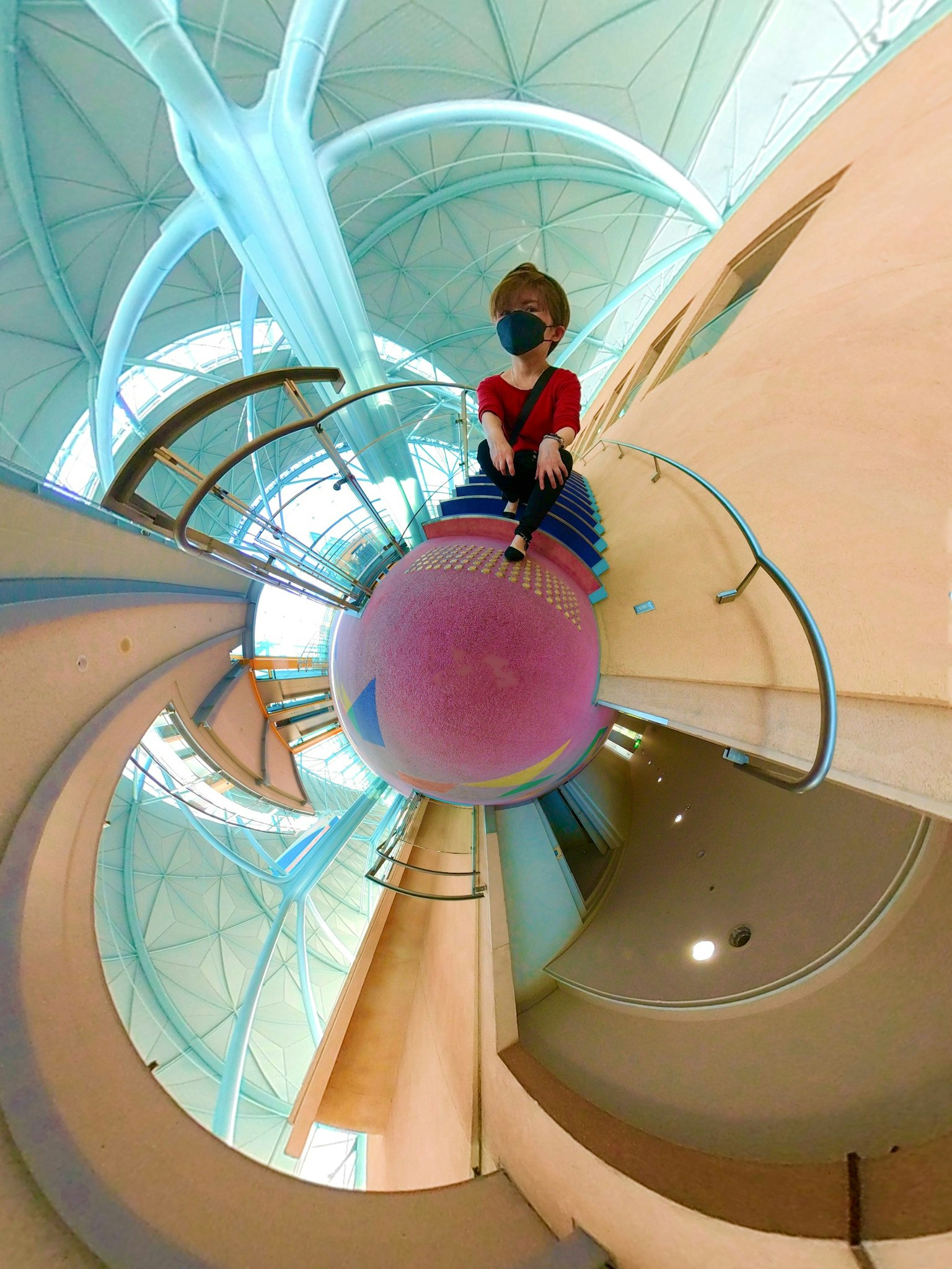 Une personne assise sur une sphère colorée dans un cadre architectural en spirale unique