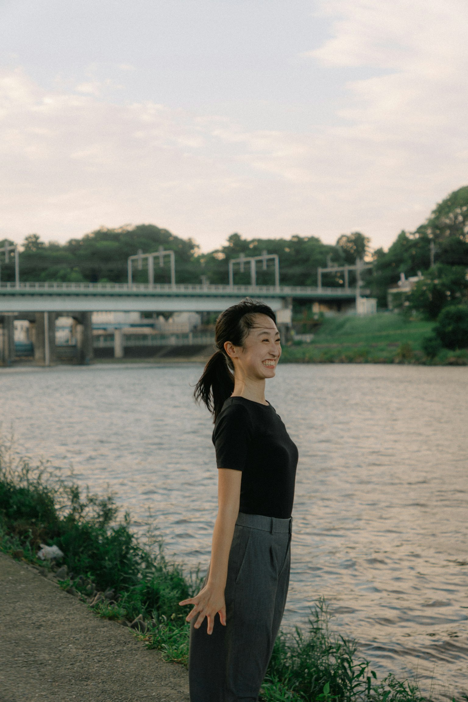 Profil latéral d'une femme posant au bord de la rivière portant un haut noir et un pantalon gris paysage serein