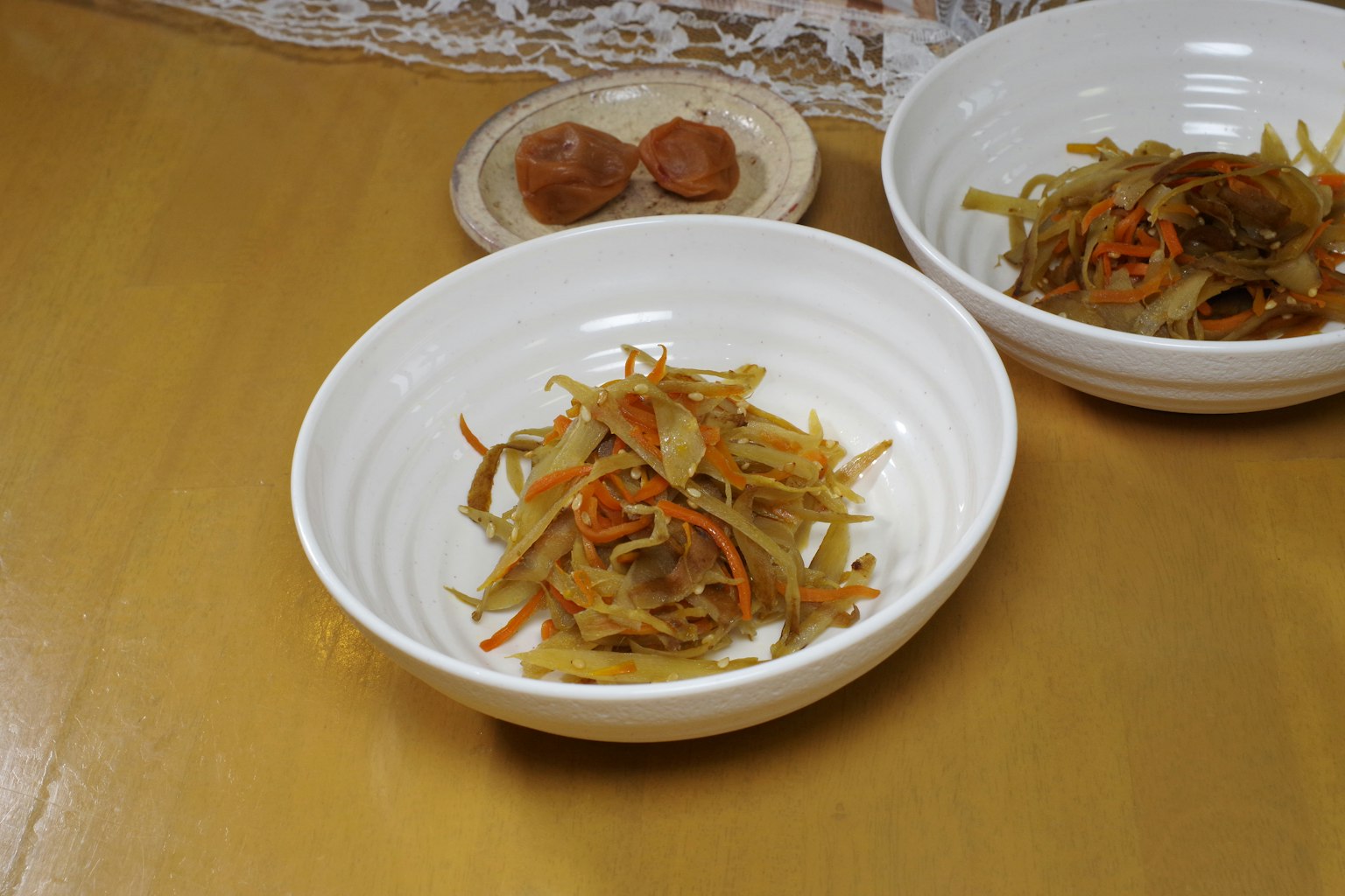 Kinpira gobo disajikan dalam mangkuk putih dengan plum acar di piring kecil