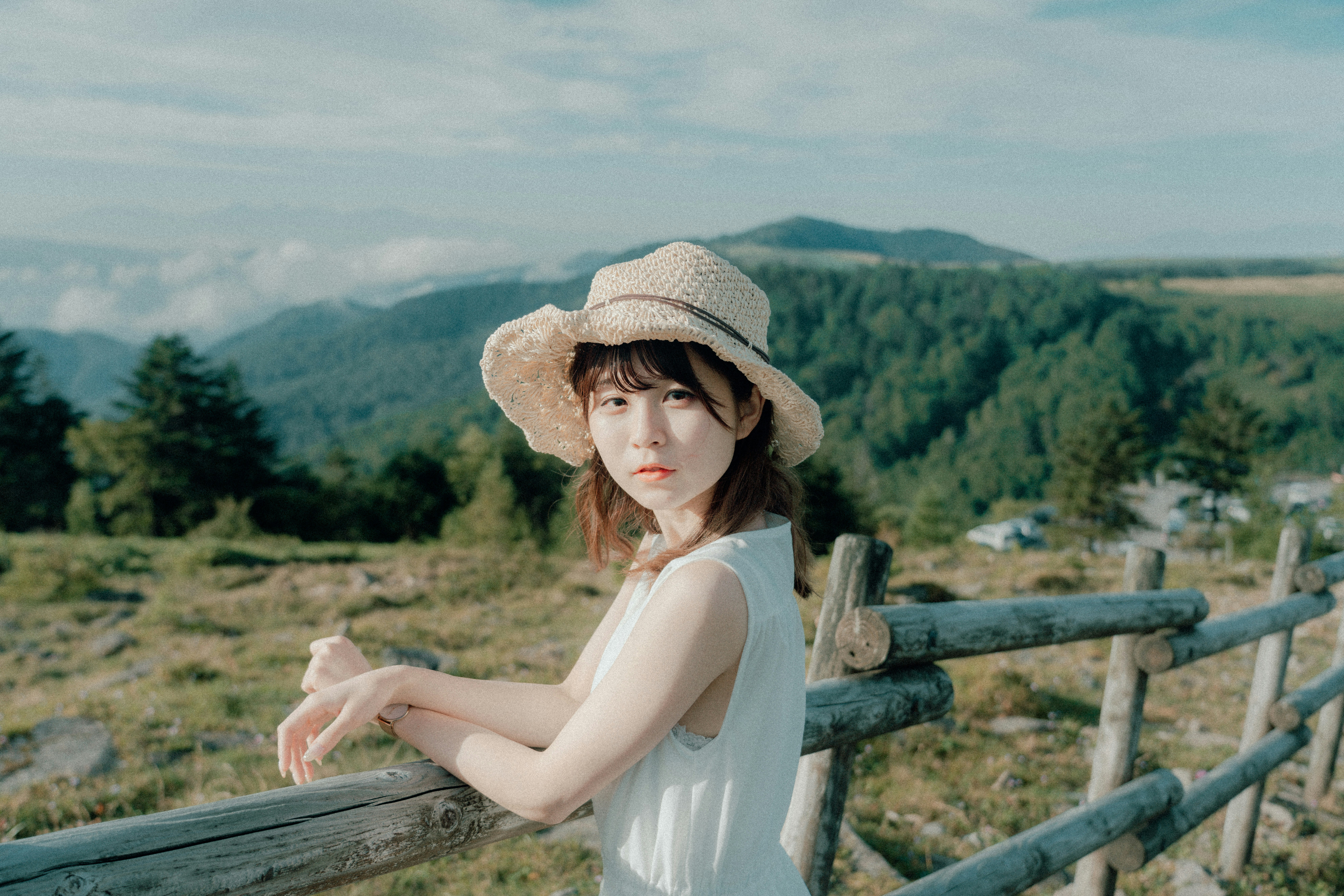 山並みを望む手すりの前で帽子をかぶった女性