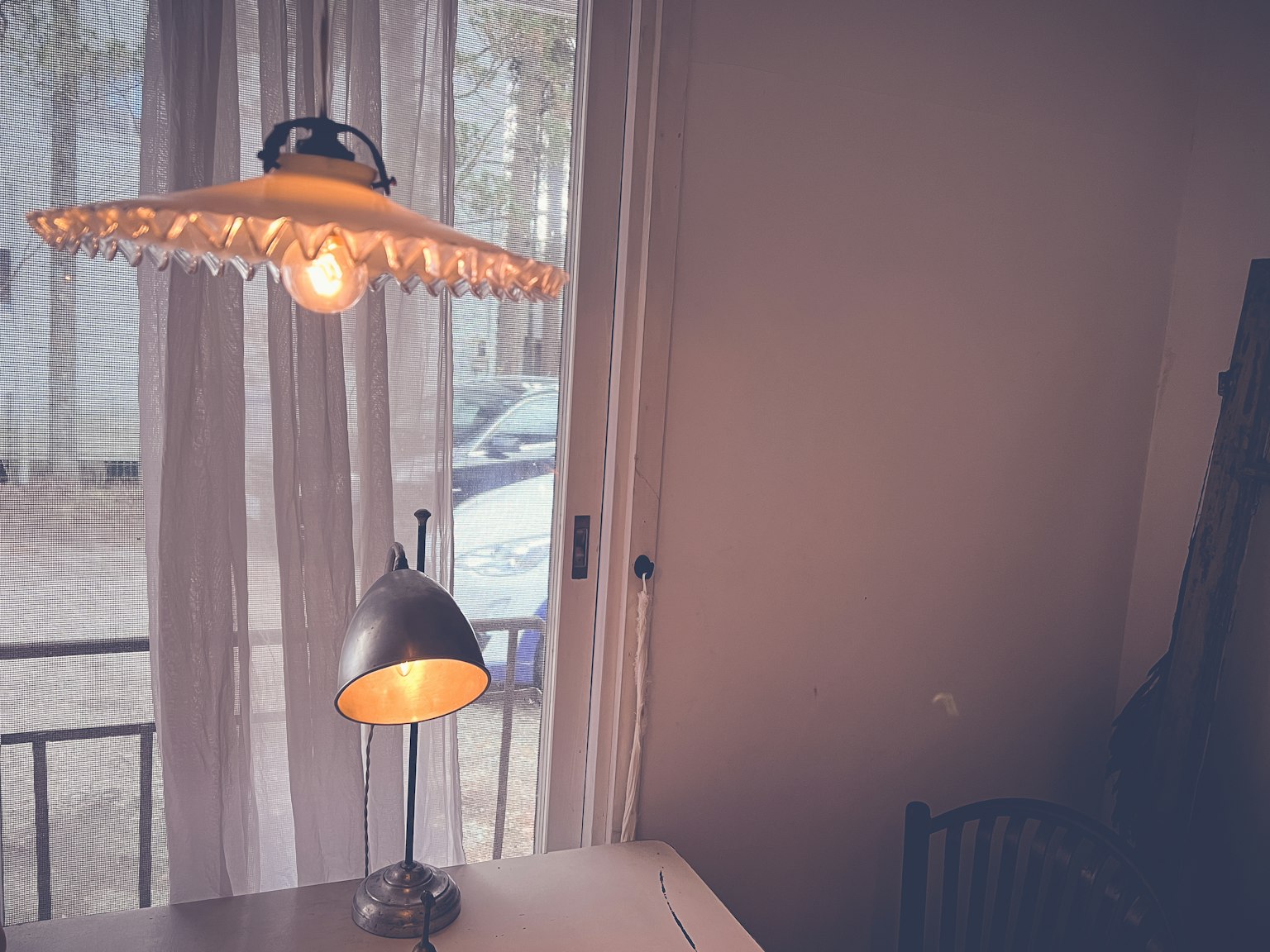 Lampada con paralume decorativo e base metallica vicino a una finestra con tende trasparenti