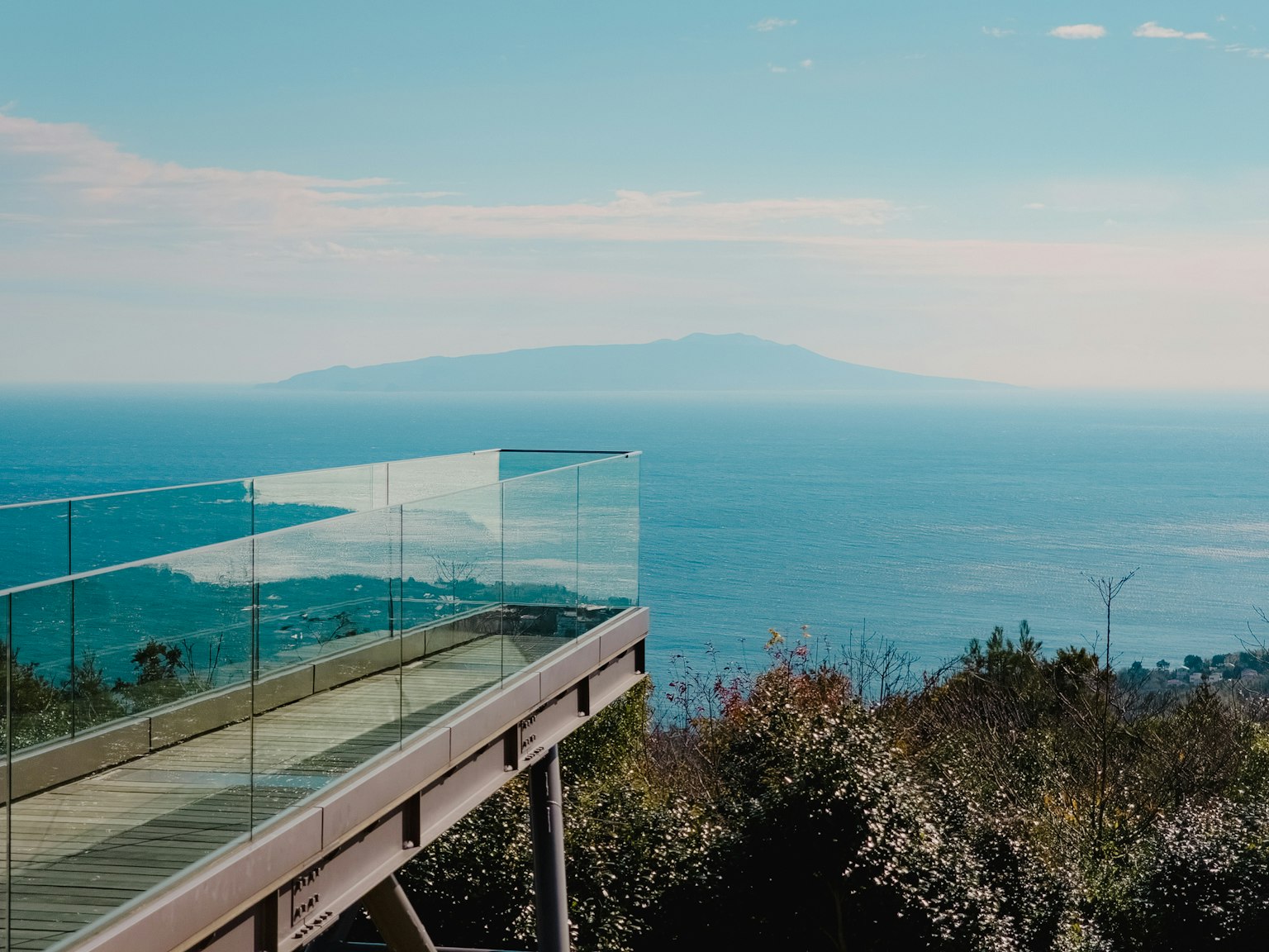 Balcón de vidrio con vista al mar y una isla lejana