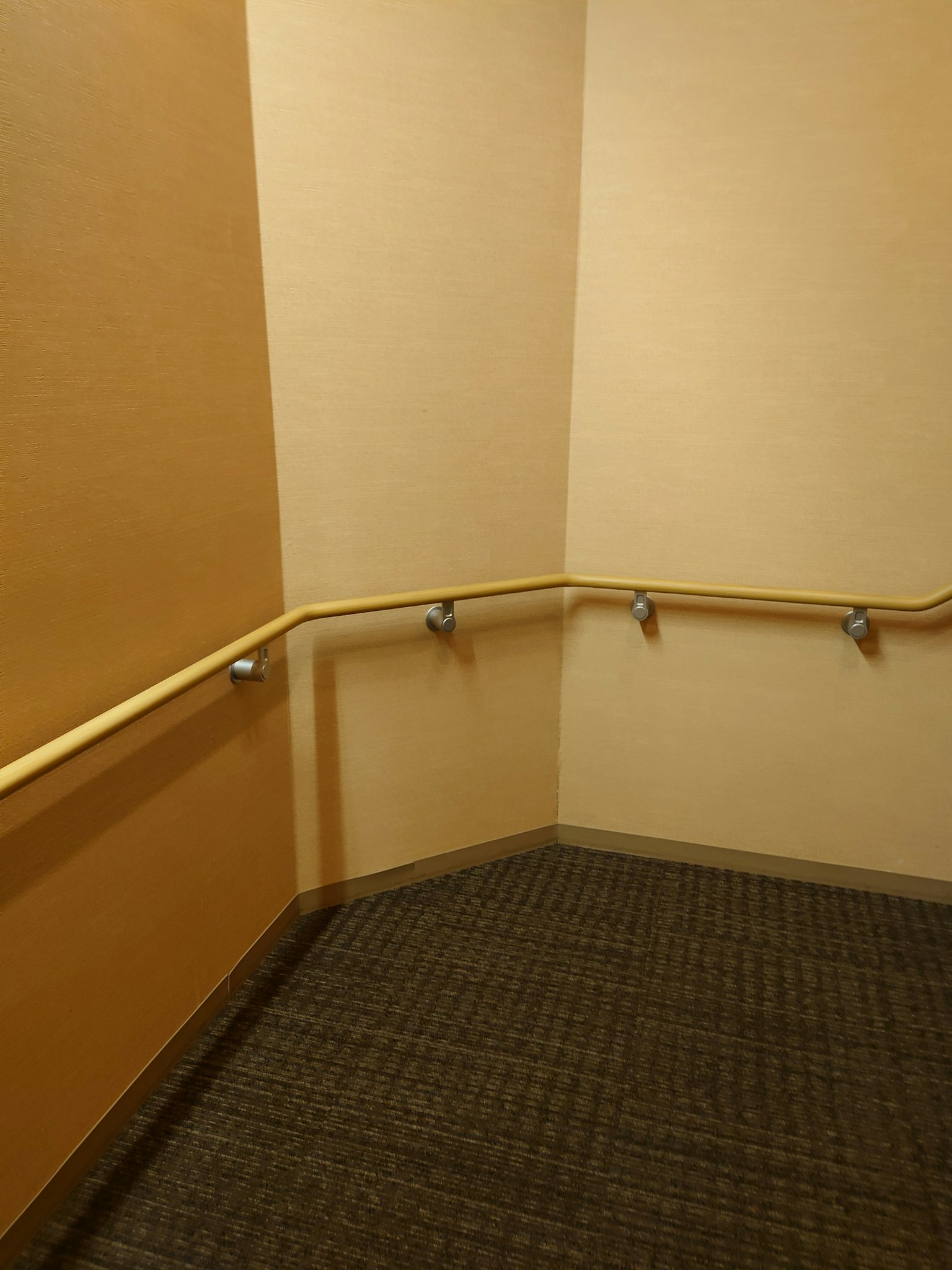 Esquina de una escalera con paredes beige y barandilla