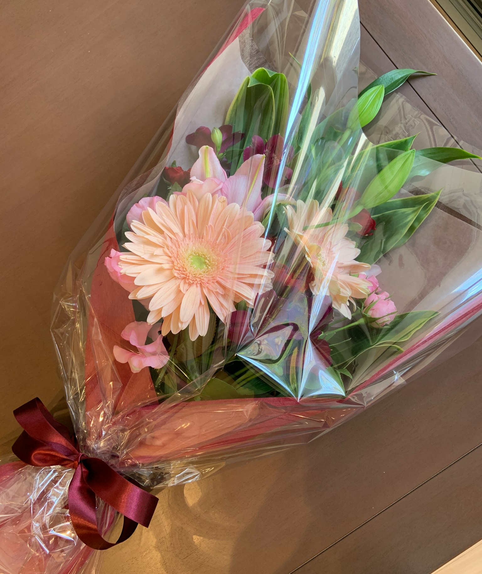 A bouquet featuring pink flowers and green leaves wrapped in clear plastic