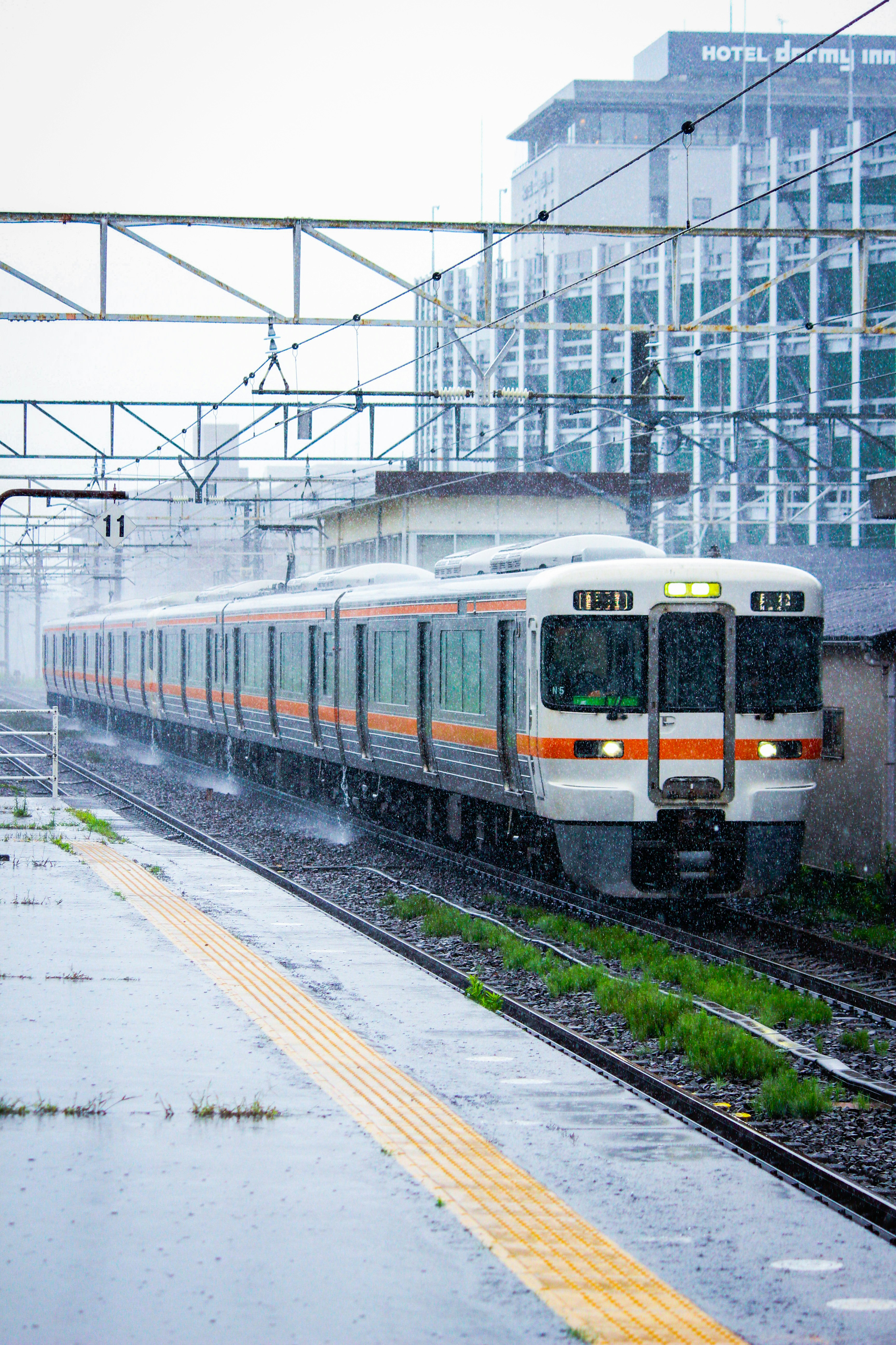 大雨の中を走る電車と線路沿いの駅ホーム