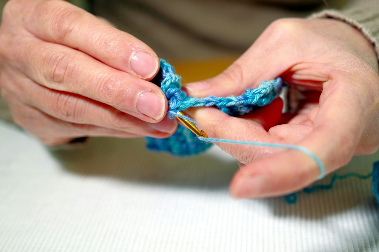Nahaufnahme von Händen, die mit blauer Wolle häkeln