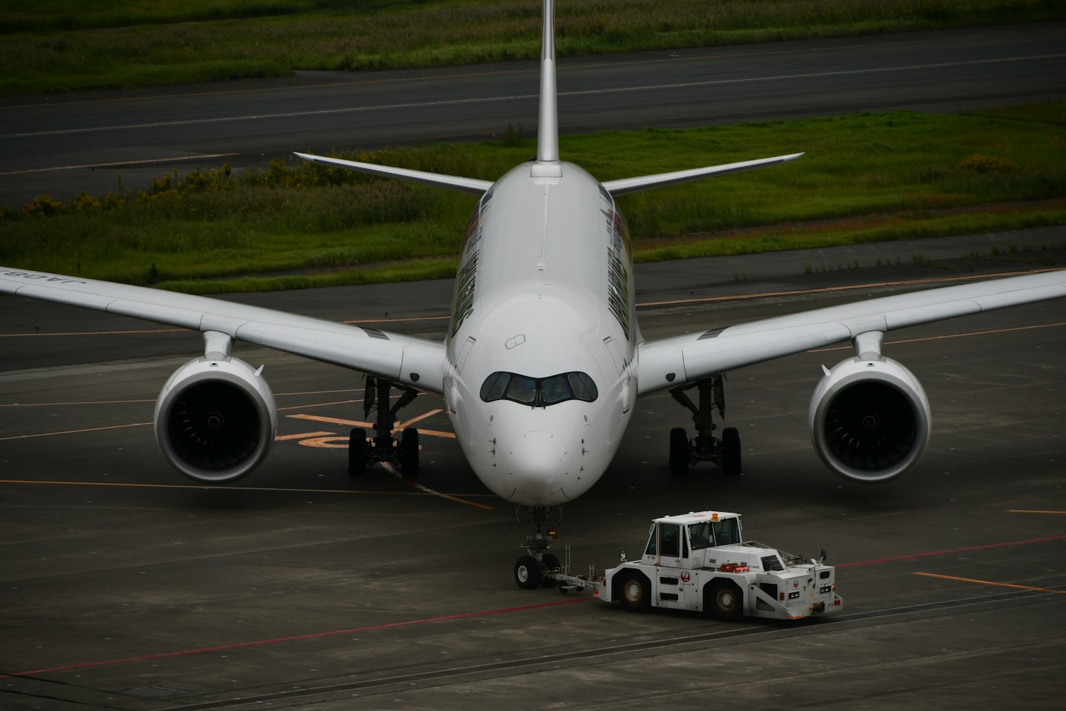 Un aereo passeggeri bianco parcheggiato sulla pista con un trattore di rimorchio davanti