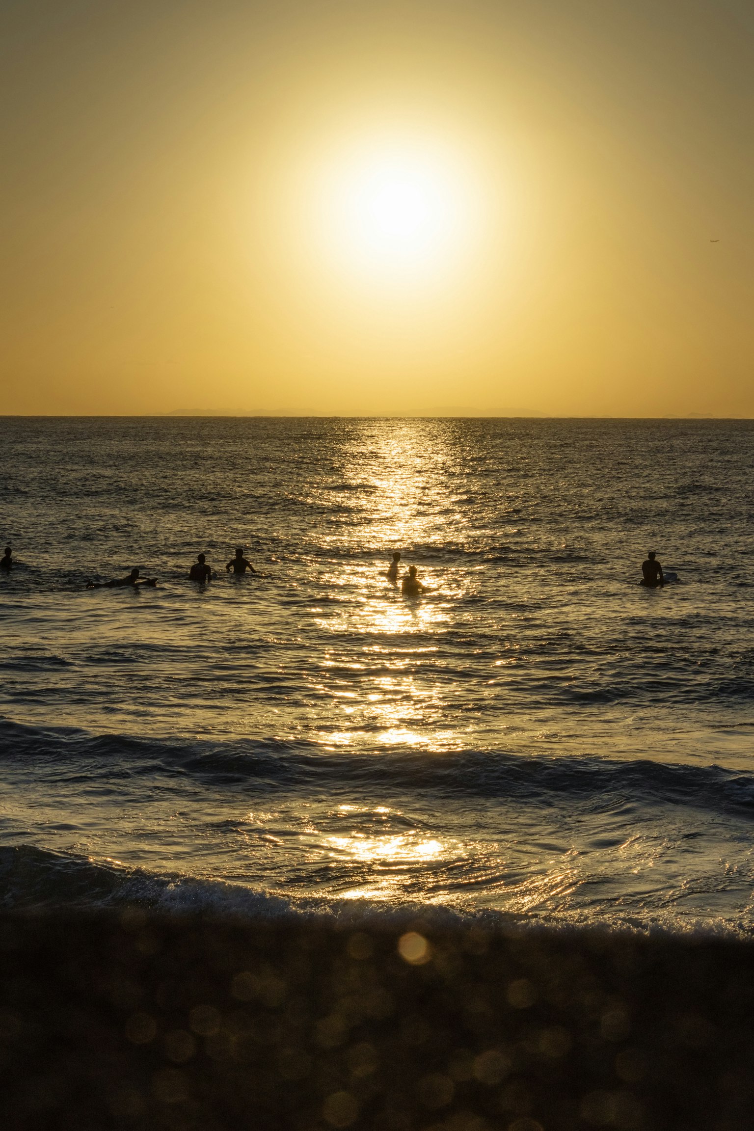 Silhouetten von Menschen, die im Ozean bei Sonnenuntergang surfen
