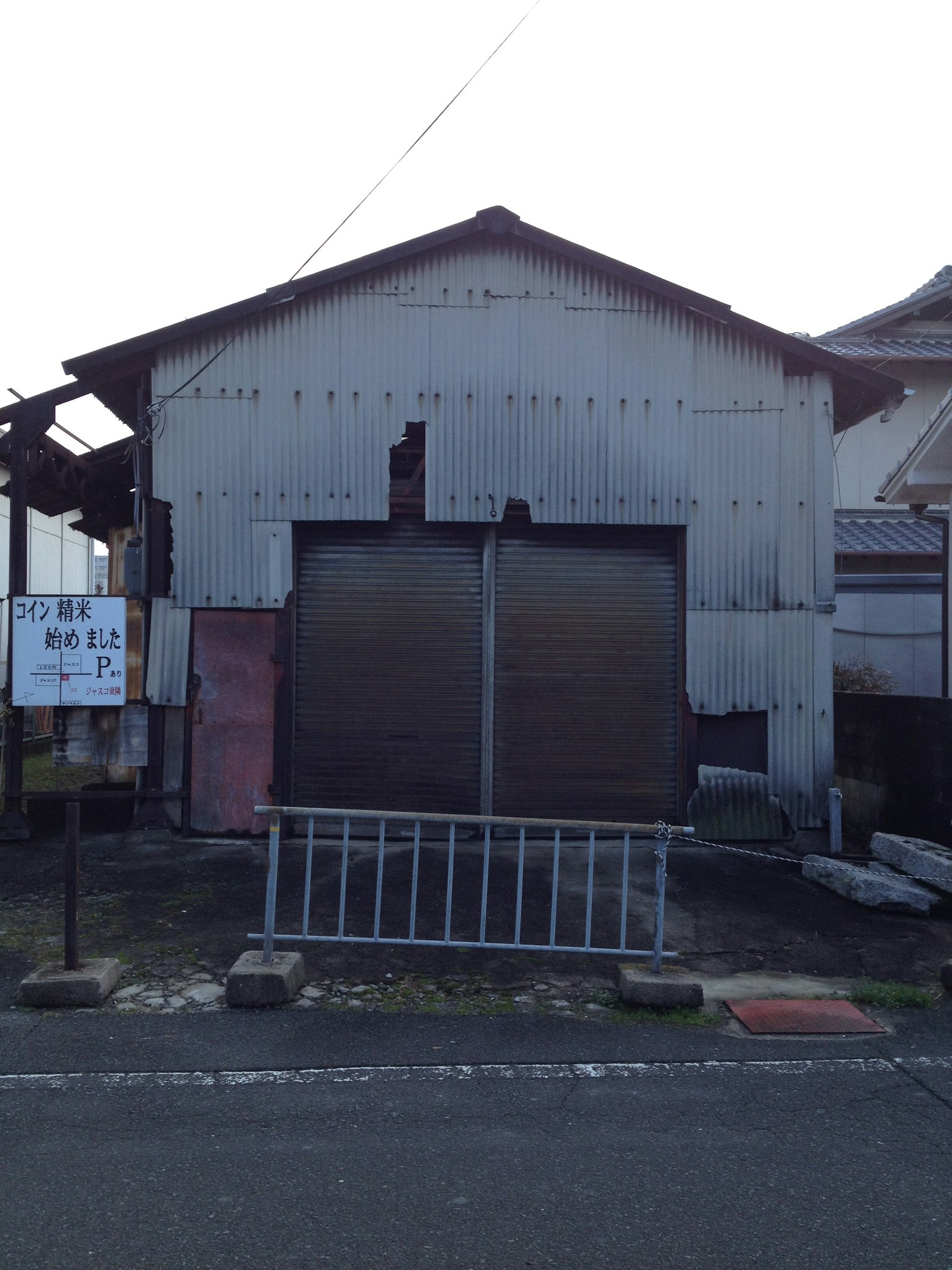 Eksterior gudang metal tua dengan fasad berkarat dan dua shutter besar dekat tangga