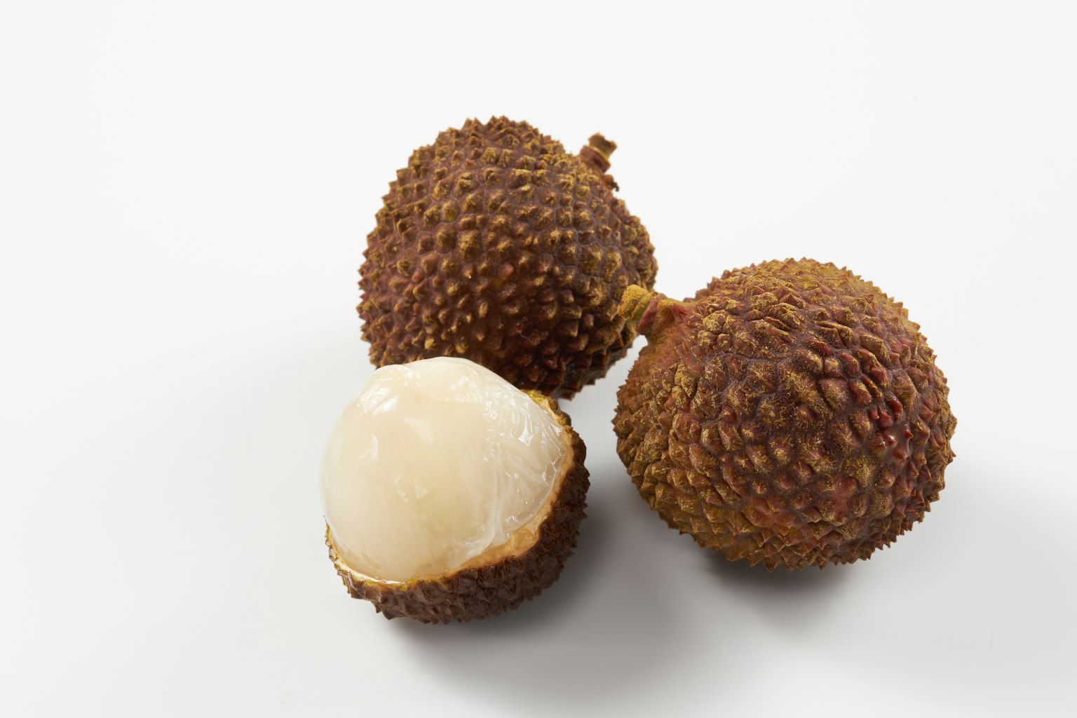 Three lychees on a white background one peeled showing the translucent flesh