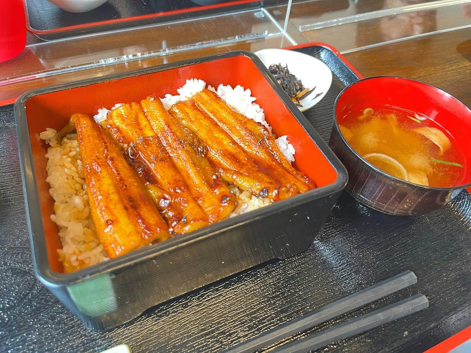 美味的鳗鱼饭在红色便当盒中盛放，配有米饭和涂抹酱汁的鳗鱼