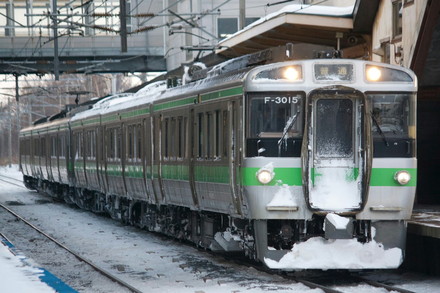 Treno verde e argento fermo su binari coperti di neve