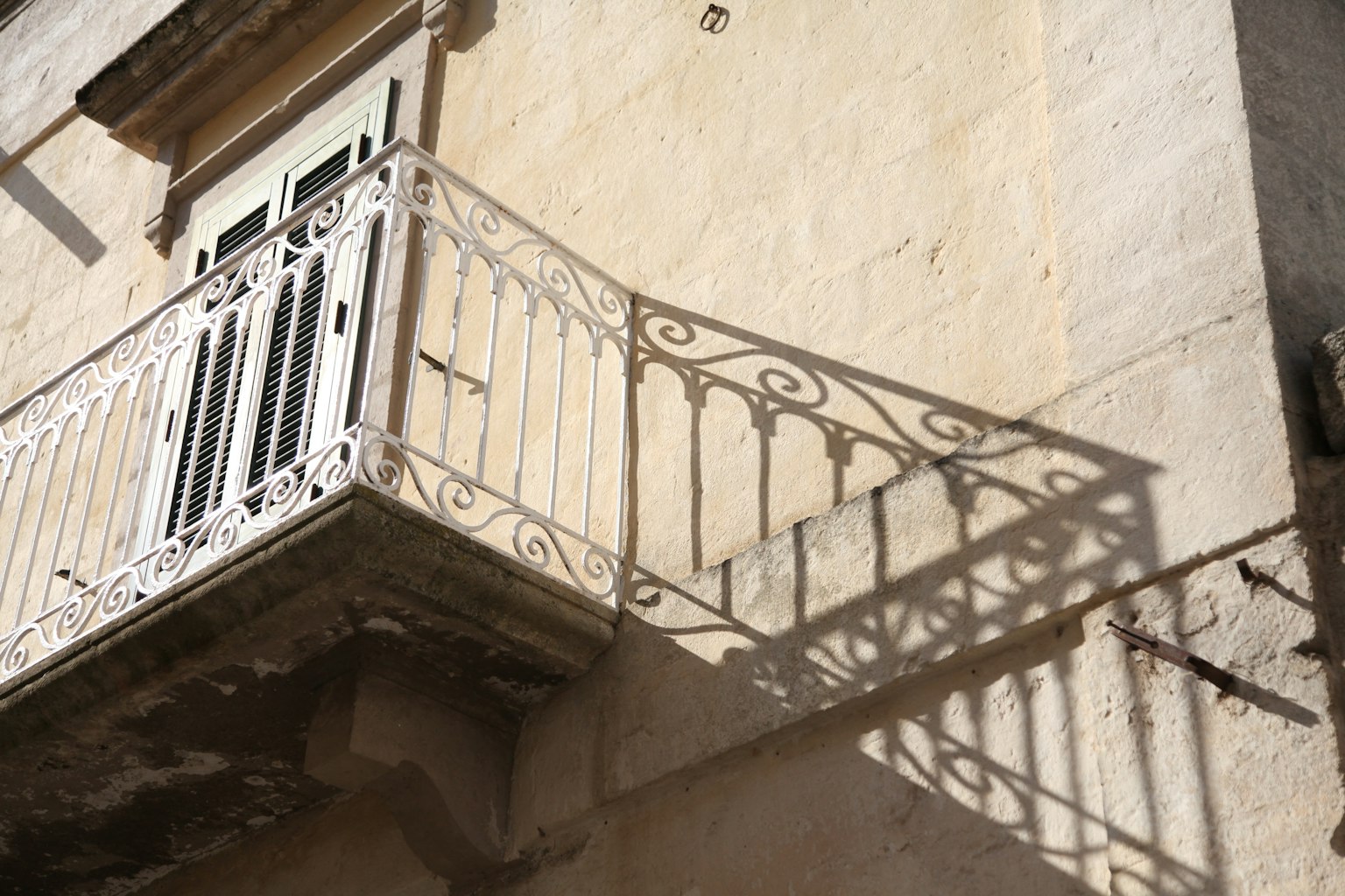 Balcon blanc projetant des ombres complexes sur un mur en pierre
