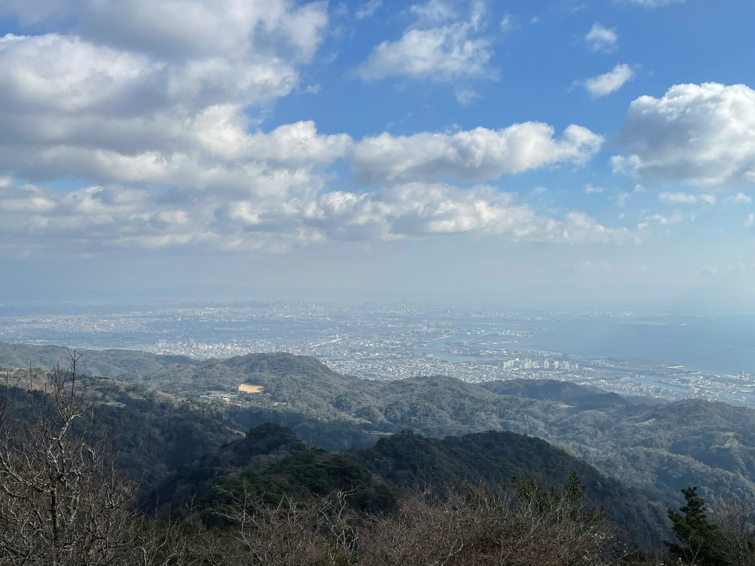Mountain landscape with blue sky and clouds green trees in the foreground distant city view