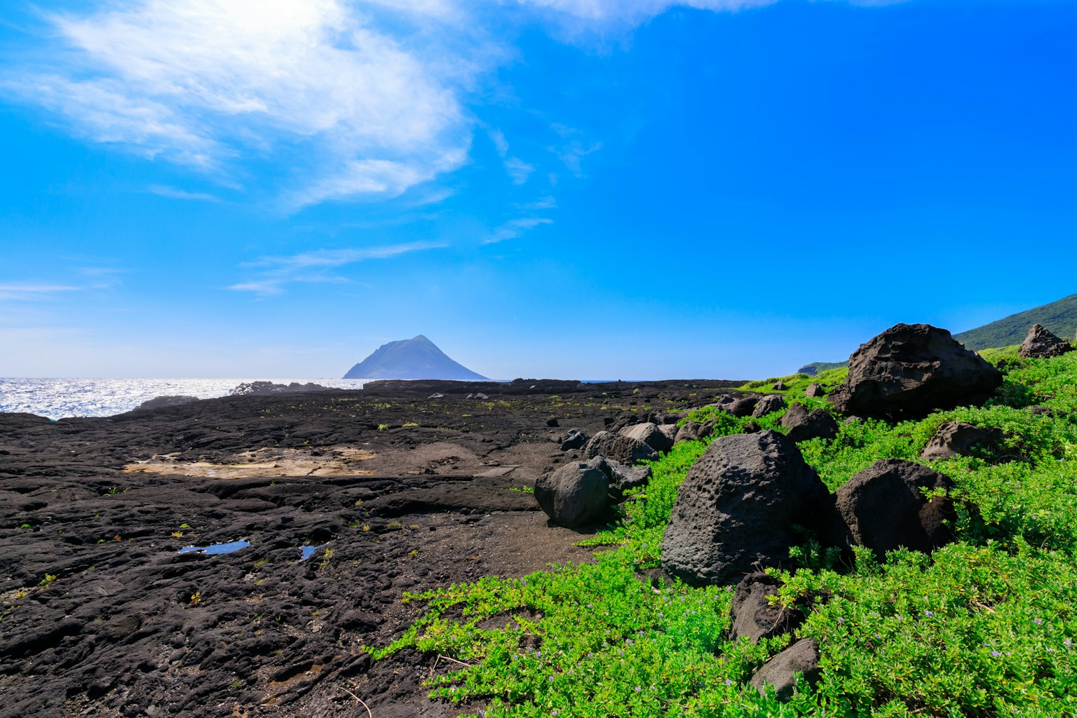 藍天與綠色植被的海岸風景，遠處有一座火山山