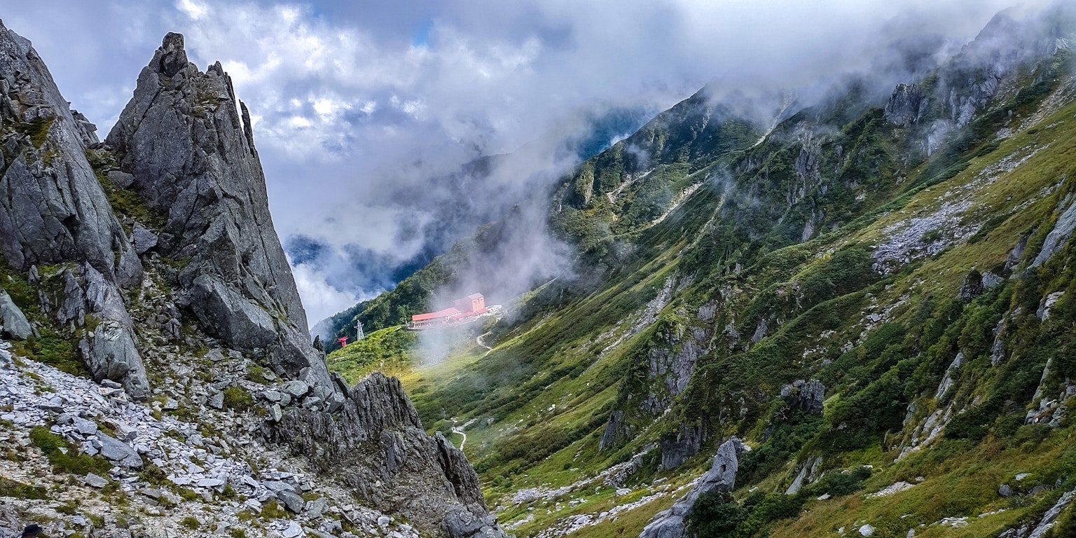 Panoramablick auf ein Bergtal mit felsigen Formationen und üppigem Grün unter bewölktem Himmel