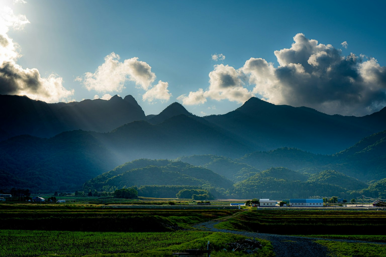 ทุ่งหญ้าสีเขียวและภูเขาใต้ท้องฟ้าสีฟ้าพร้อมเมฆ