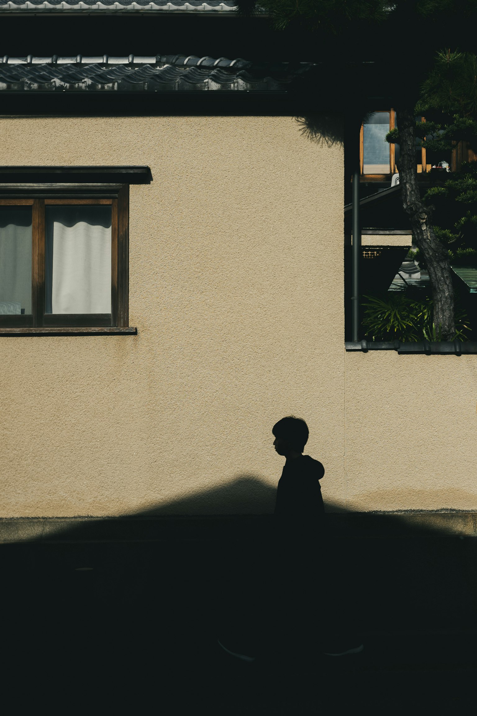 Un bambino che cammina nell'ombra vicino a una casa con una finestra