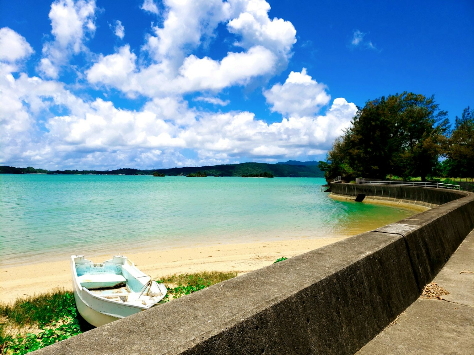 美麗的海灘景觀，藍色的水和白色的雲，包含一隻小船和石牆