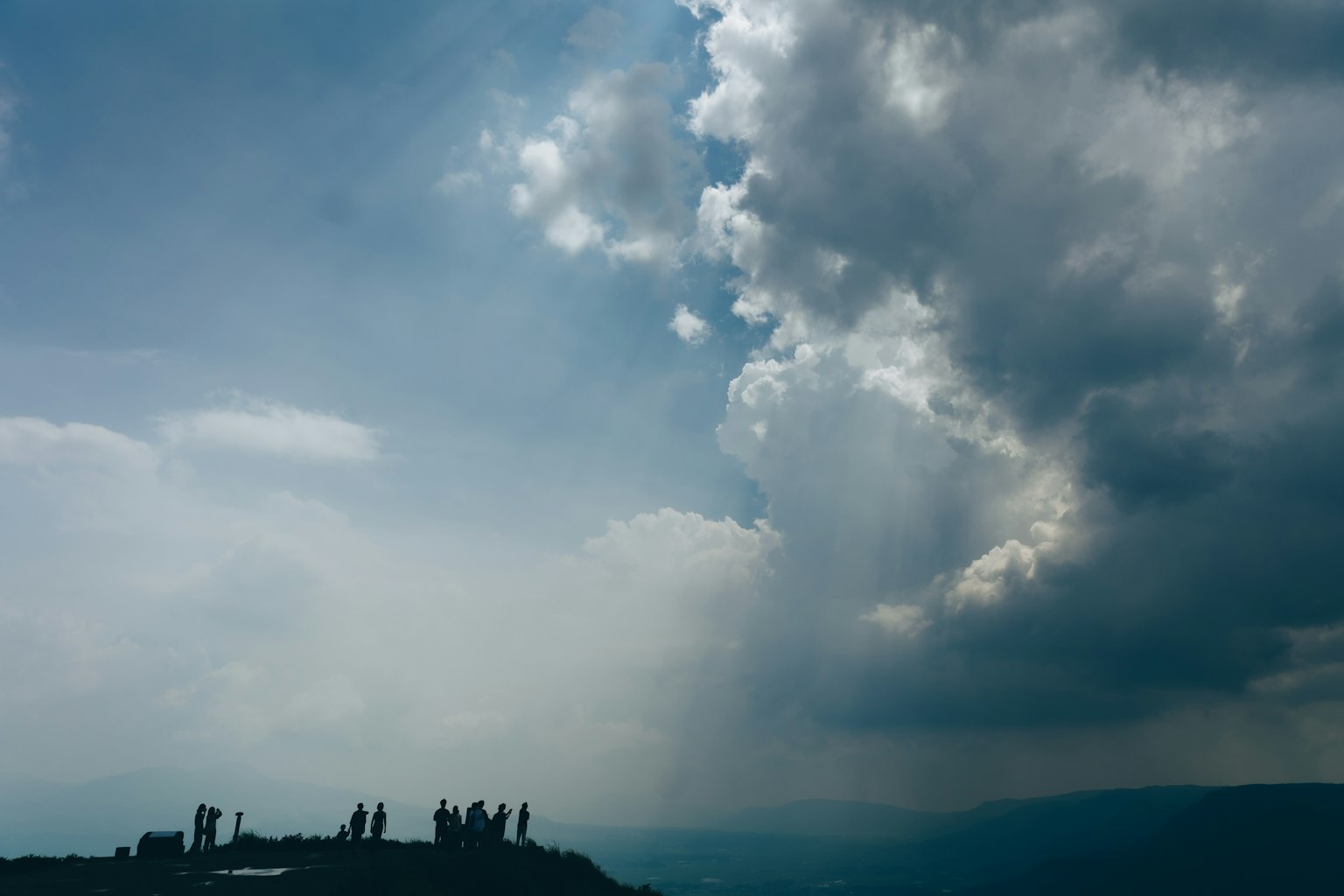 Silhouette di persone contro un cielo nuvoloso con montagne lontane visibili