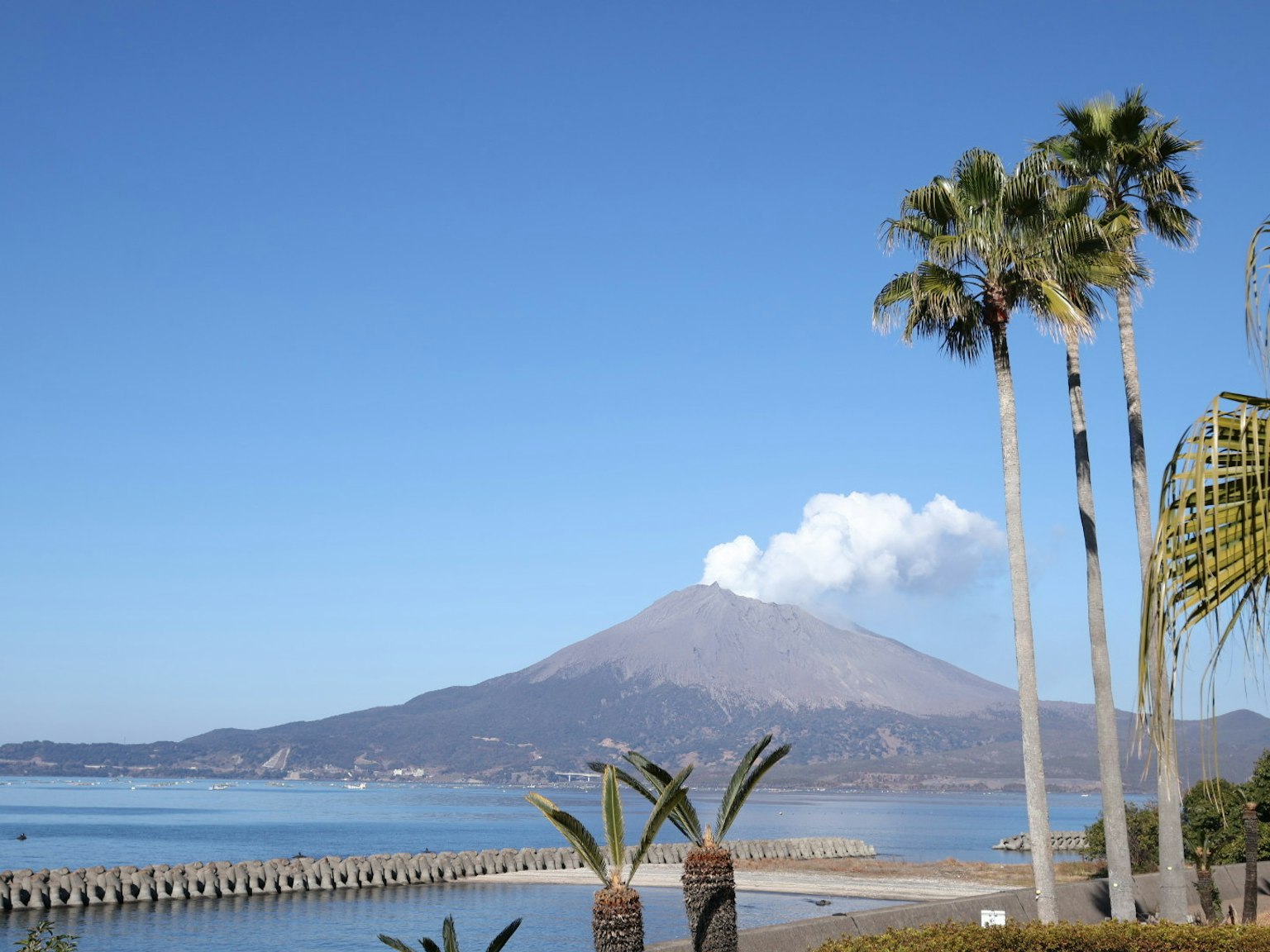Vista escénica de un volcán rodeado de cielo azul y océano con palmeras