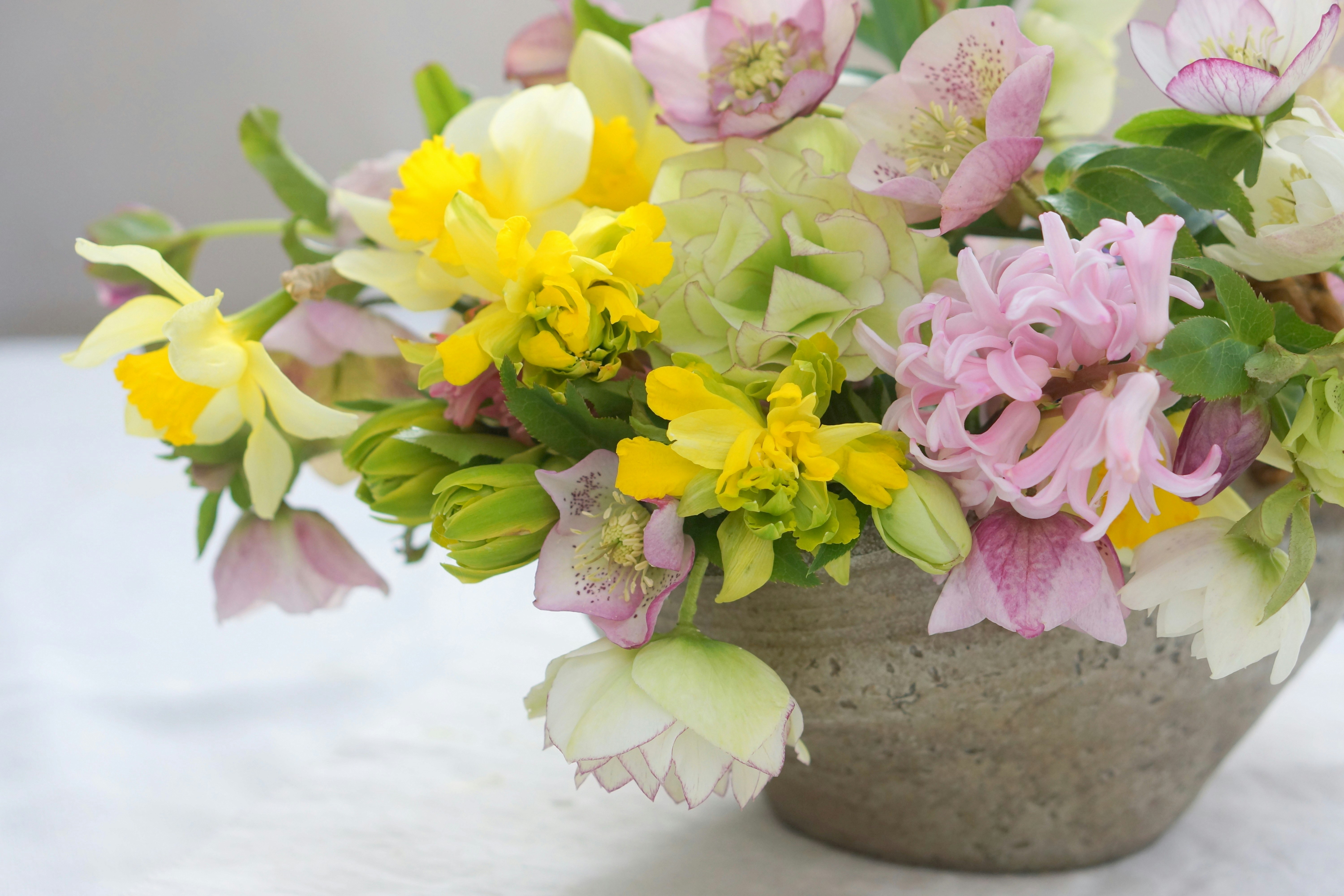 ピンクとイエローの花が入ったセメント調の鉢のフラワーアレンジメント