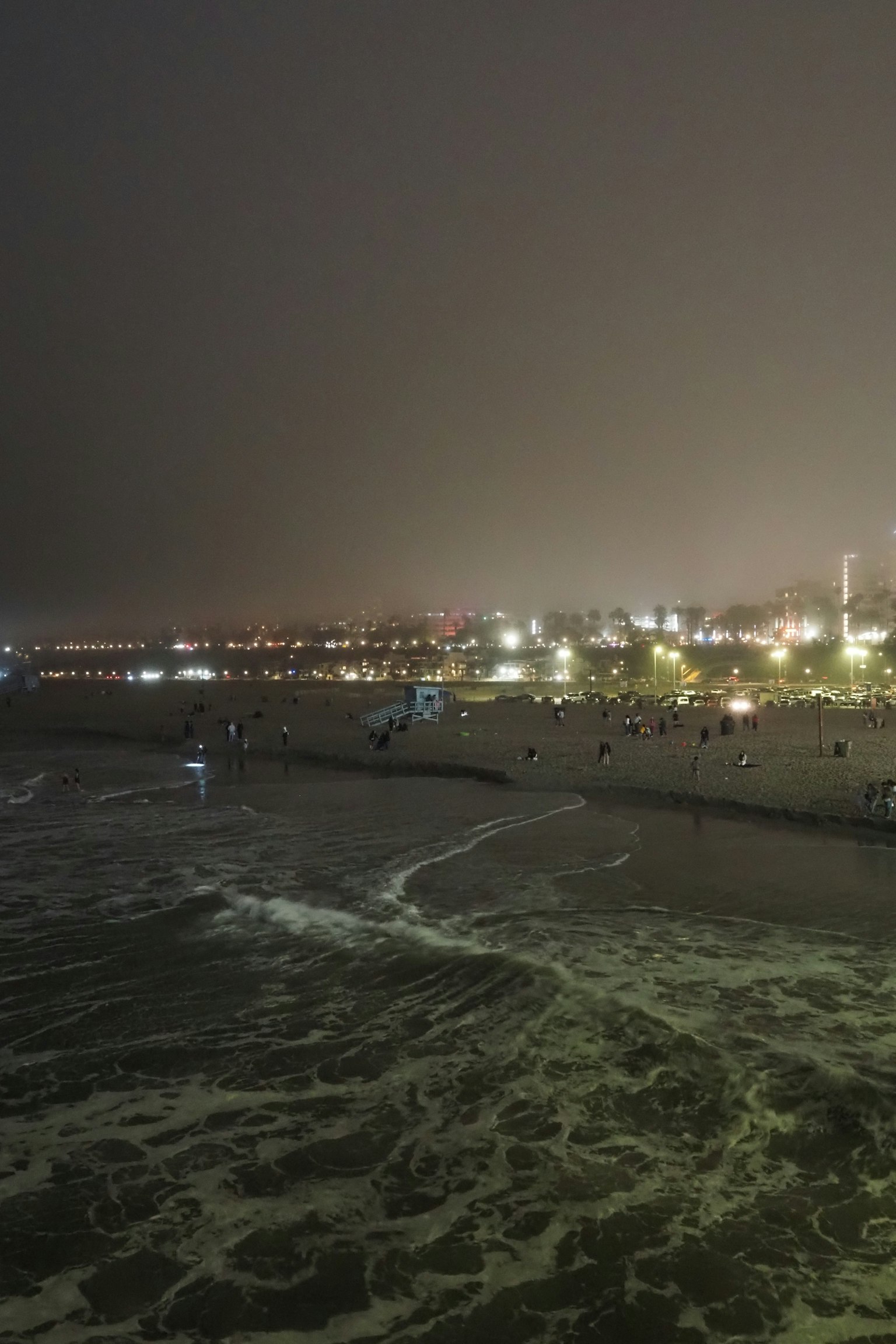 Vista nocturna de una playa con personas y olas