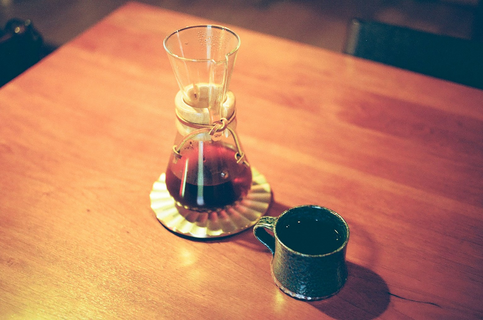Sebuah pembuat kopi dan cangkir di atas meja kayu