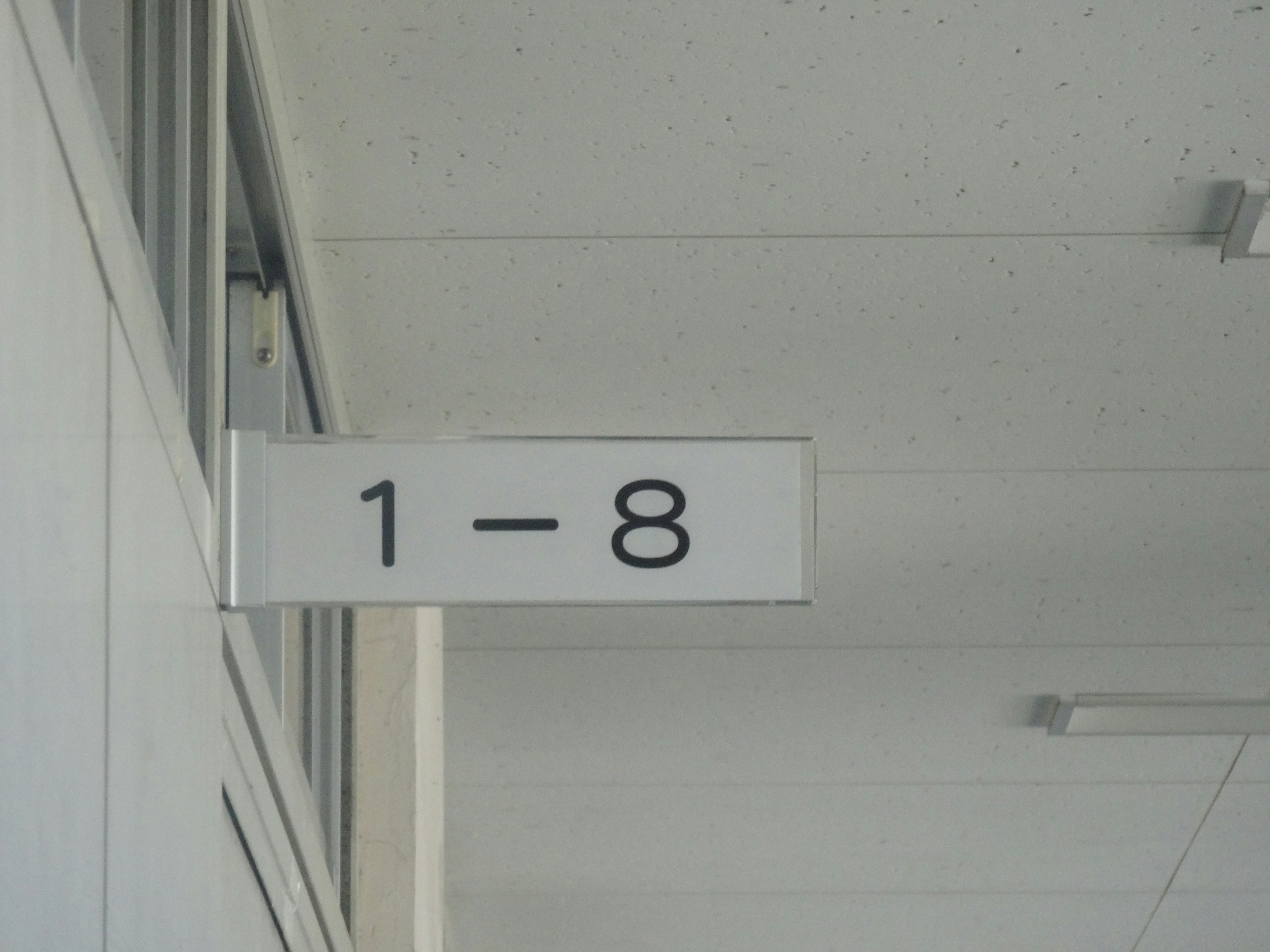 白い廊下の壁に掛かった「1-8」の番号プレート