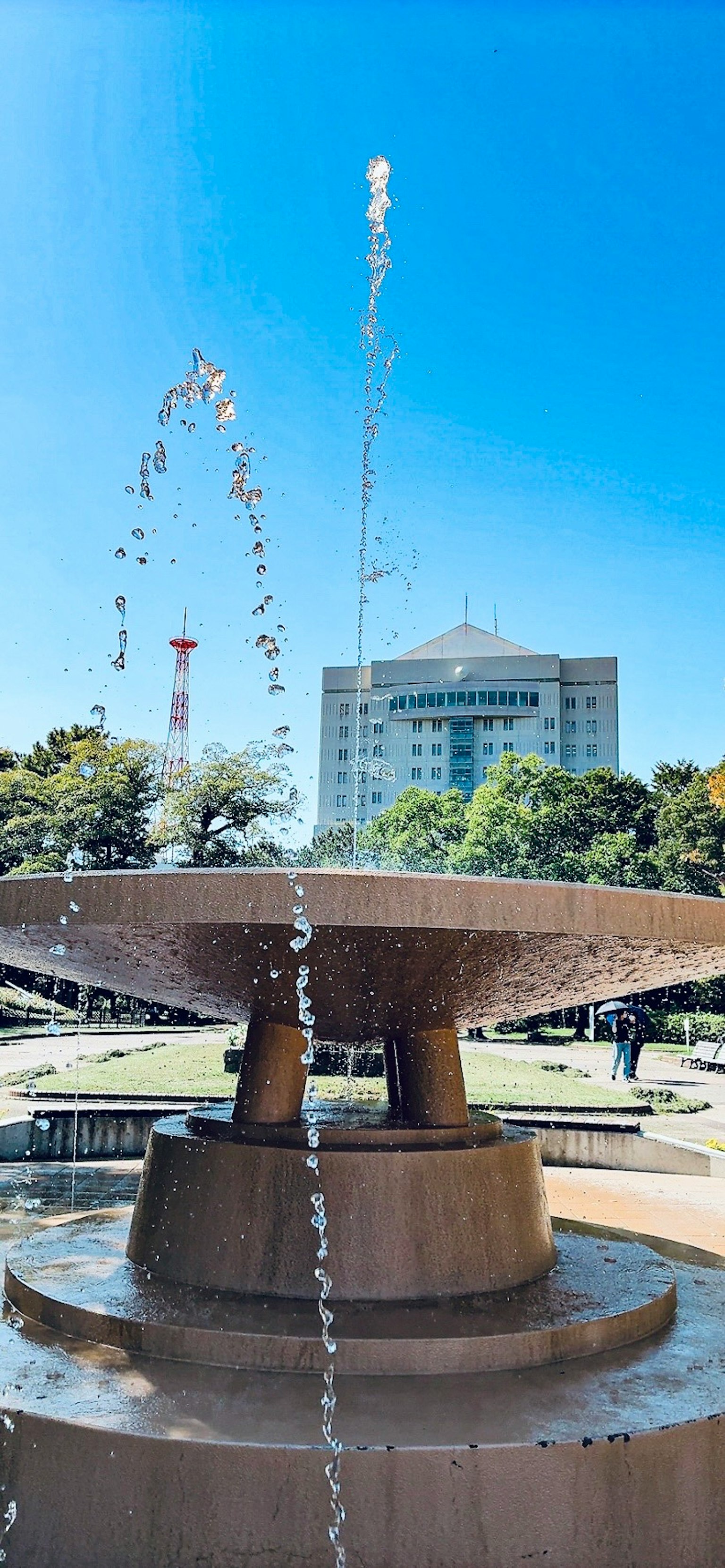 公園の噴水と青空の背景にある建物