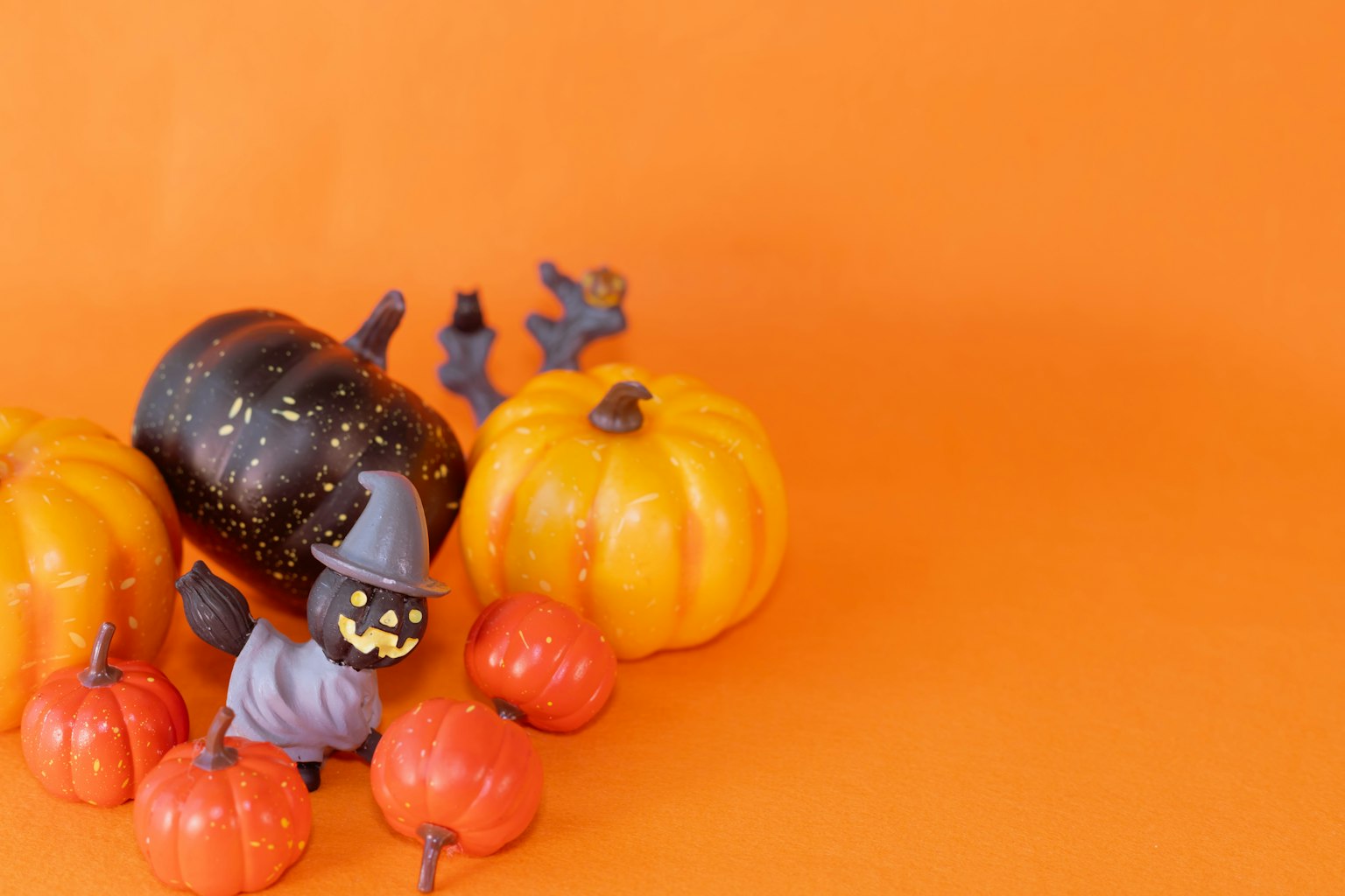 Zucche colorate e una piccola figurina di strega su uno sfondo arancione