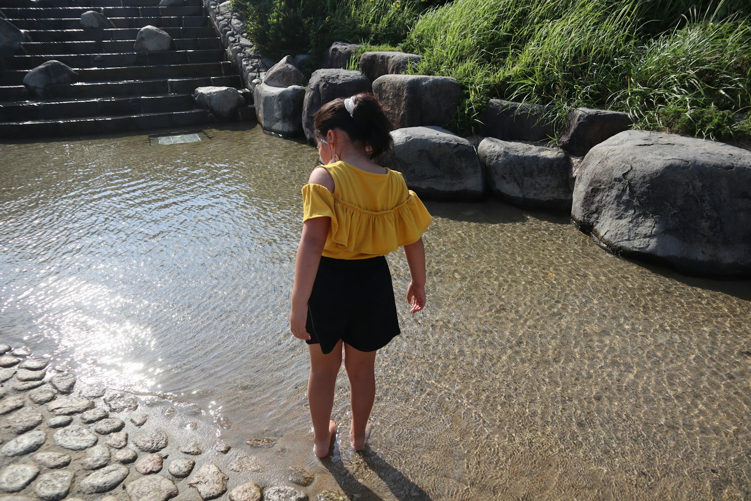 Bambina in piedi nell'acqua bassa con una maglietta gialla e pantaloni corti neri
