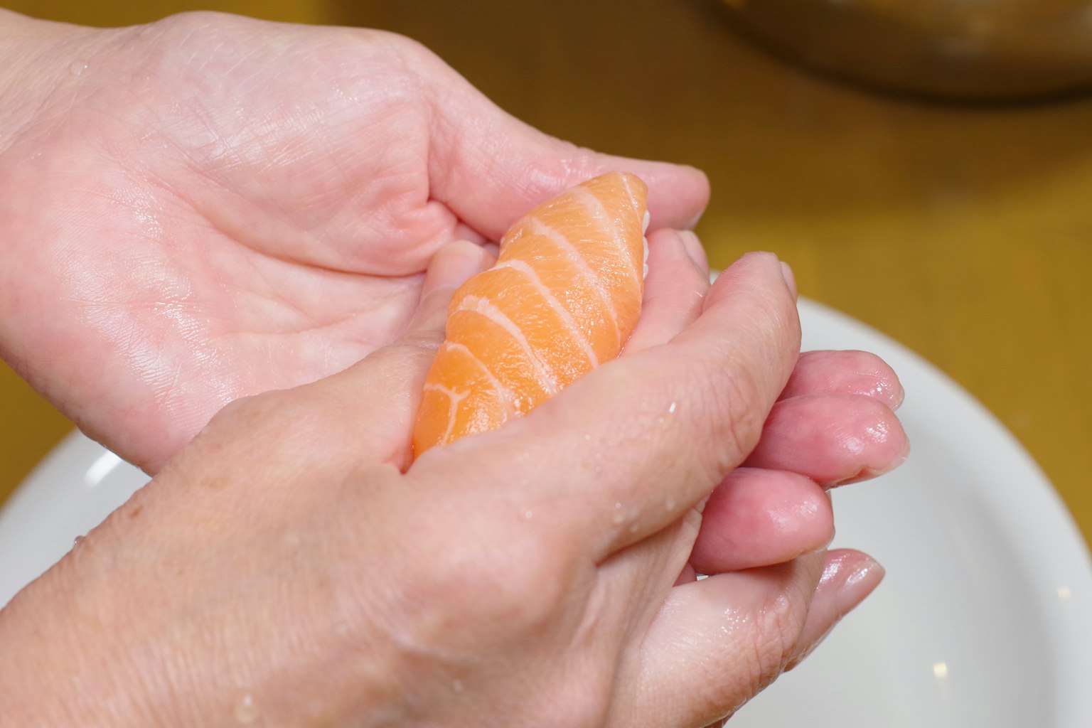 Manos moldeando un trozo de sushi de salmón