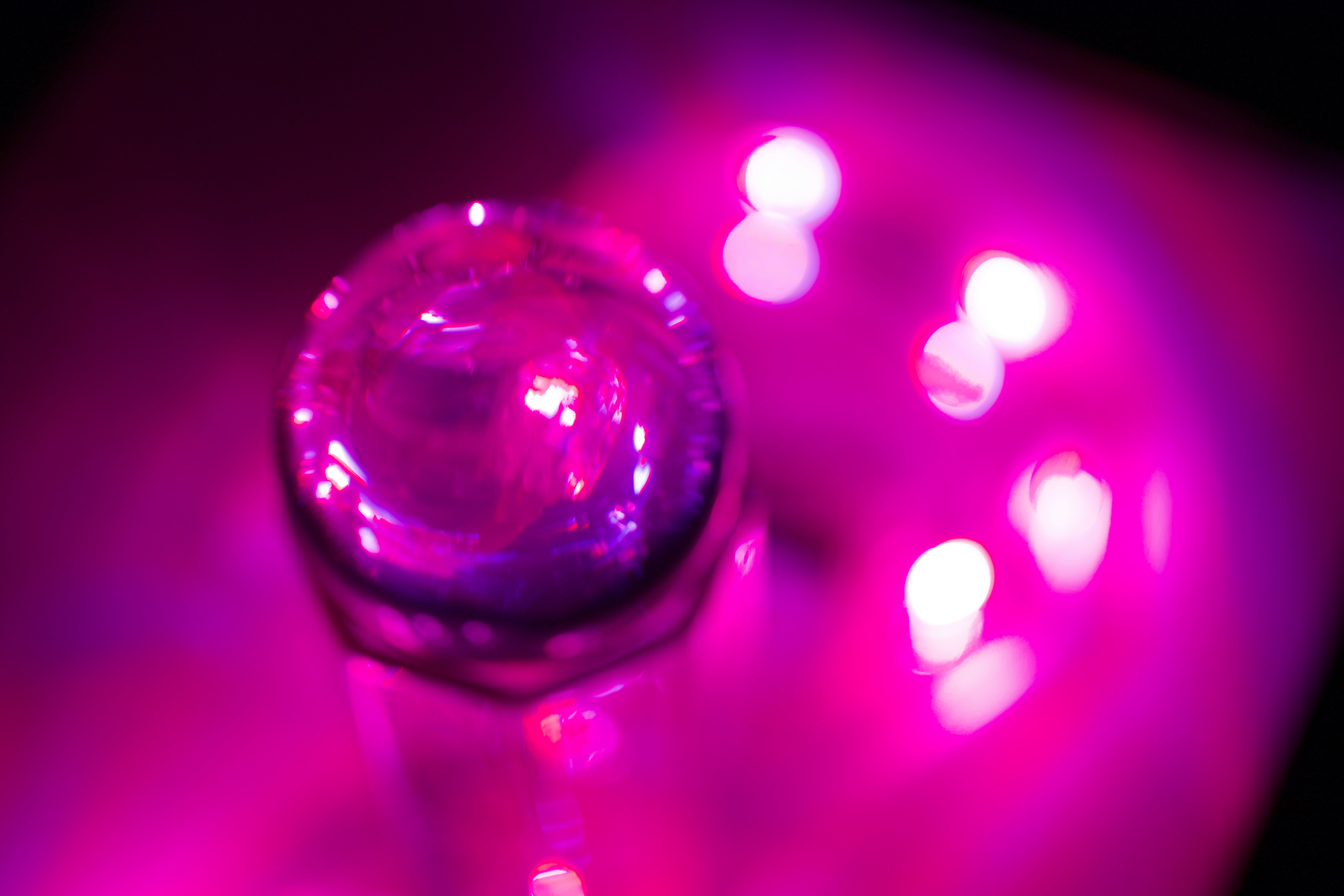 ピンクのネオン光がにじむガラス玉と光ボケの抽象的な光景