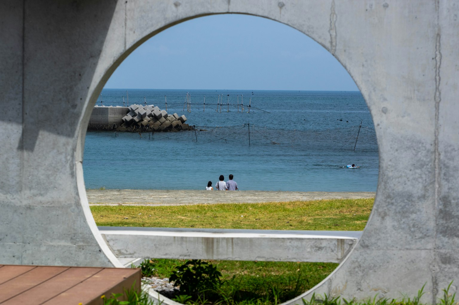 Blick durch einen runden Betrahmen auf das Meer und den Strand mit sitzenden Personen