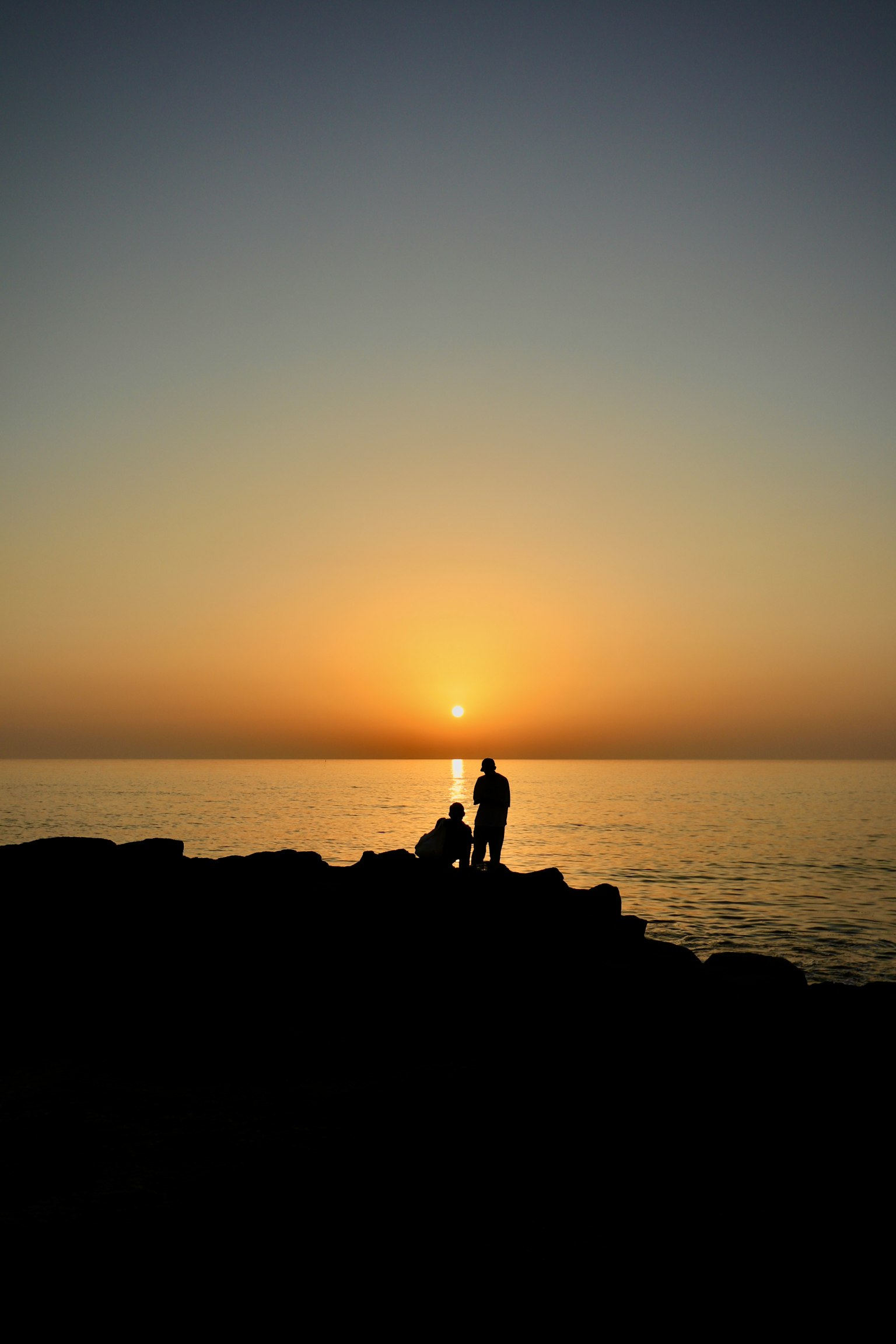 Silhouette di due persone in piedi su una scogliera al tramonto