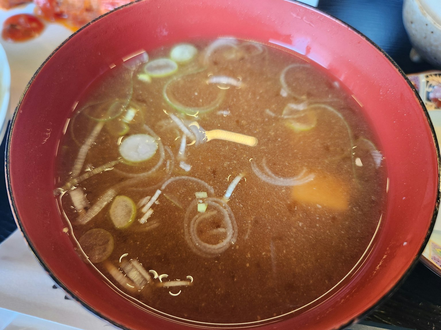 Bol de soupe dans un plat rouge avec des oignons verts et divers ingrédients