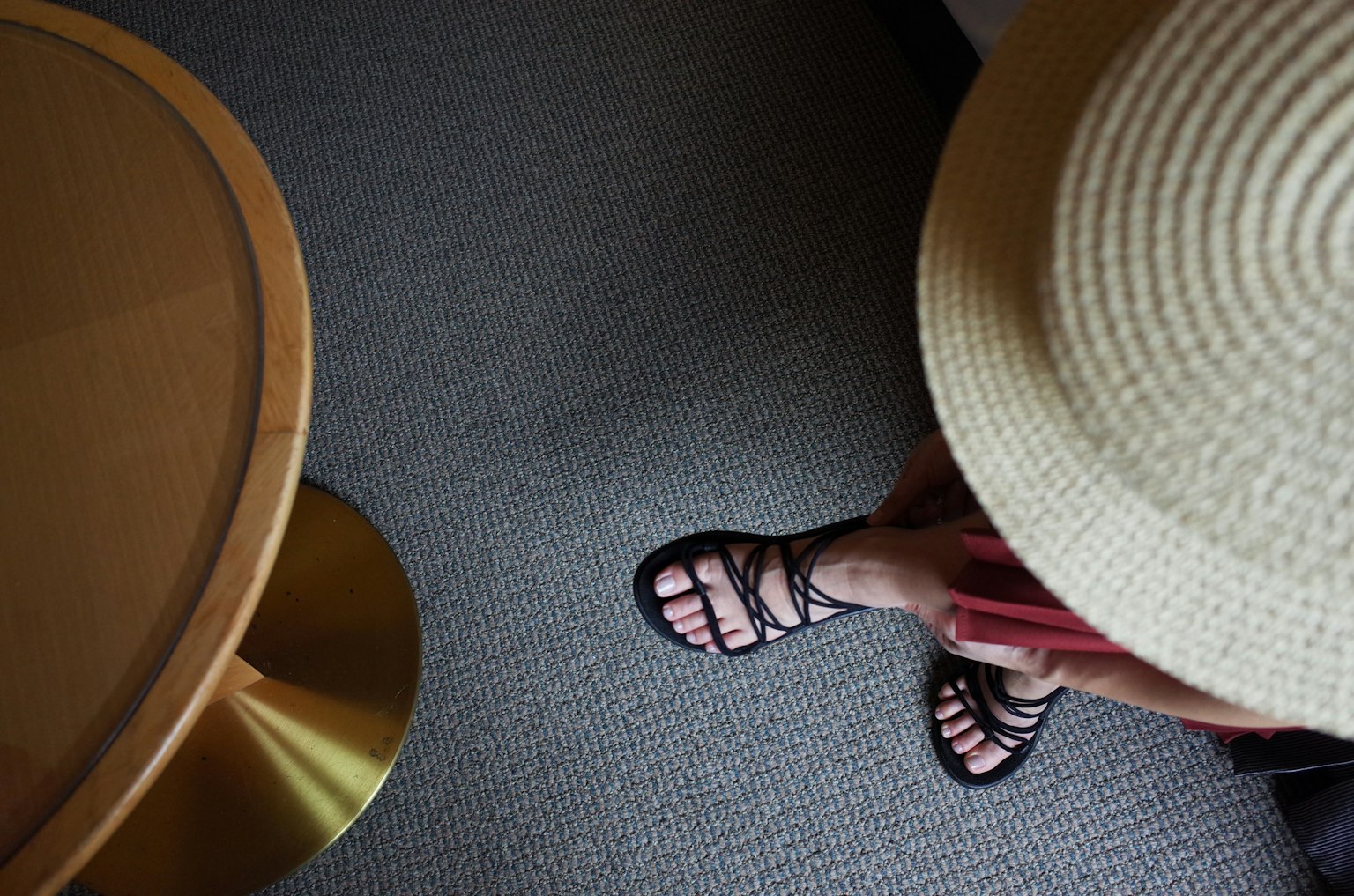 Foto de los pies de una persona usando sandalias con un sombrero de paja y una alfombra de fondo