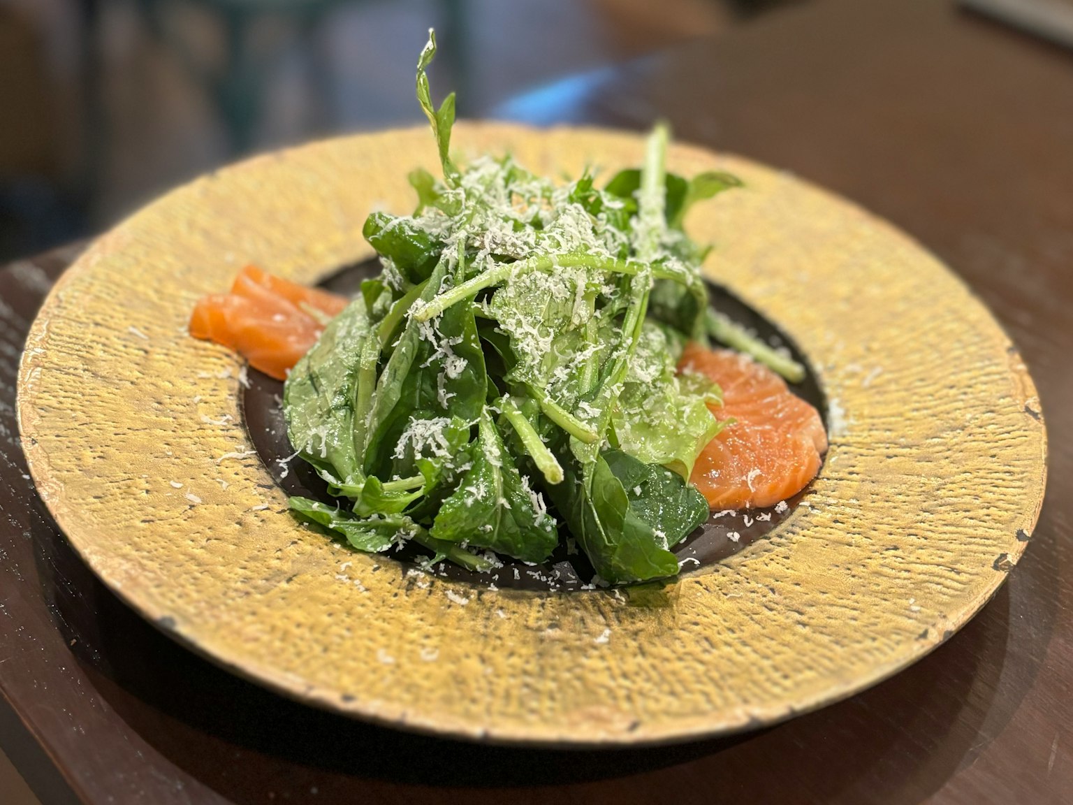 Salad được phục vụ trên đĩa vàng với lát cá hồi và rắc phô mai parmesan
