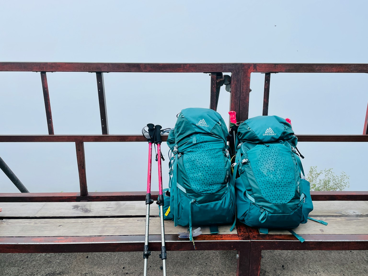兩個青色背包放在長椅上，旁邊有登山杖