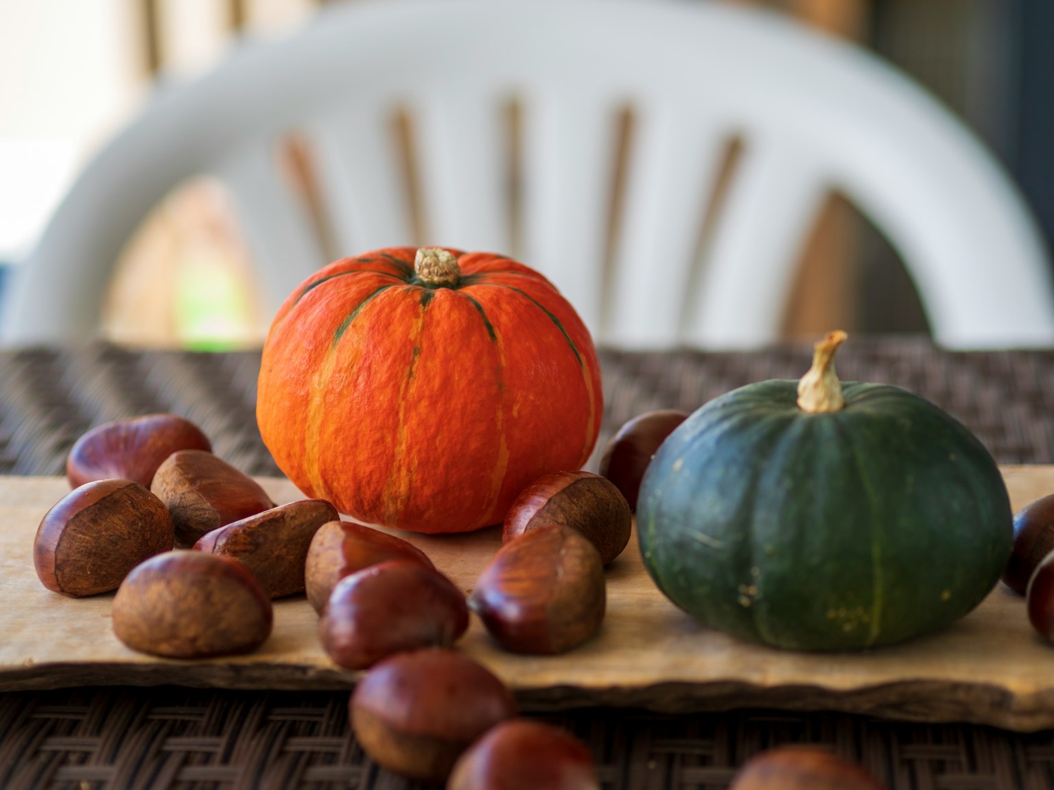 Orange Kürbis und grüner Kürbis auf einem Tisch mit verstreuten Kastanien