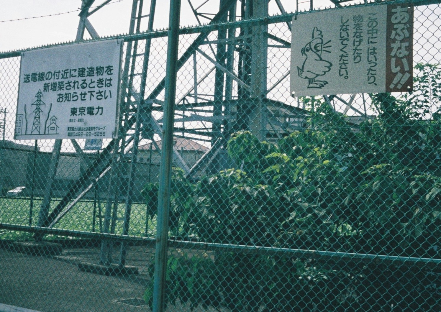 フェンス越しの線路と鉄骨の高架、看板のある風景