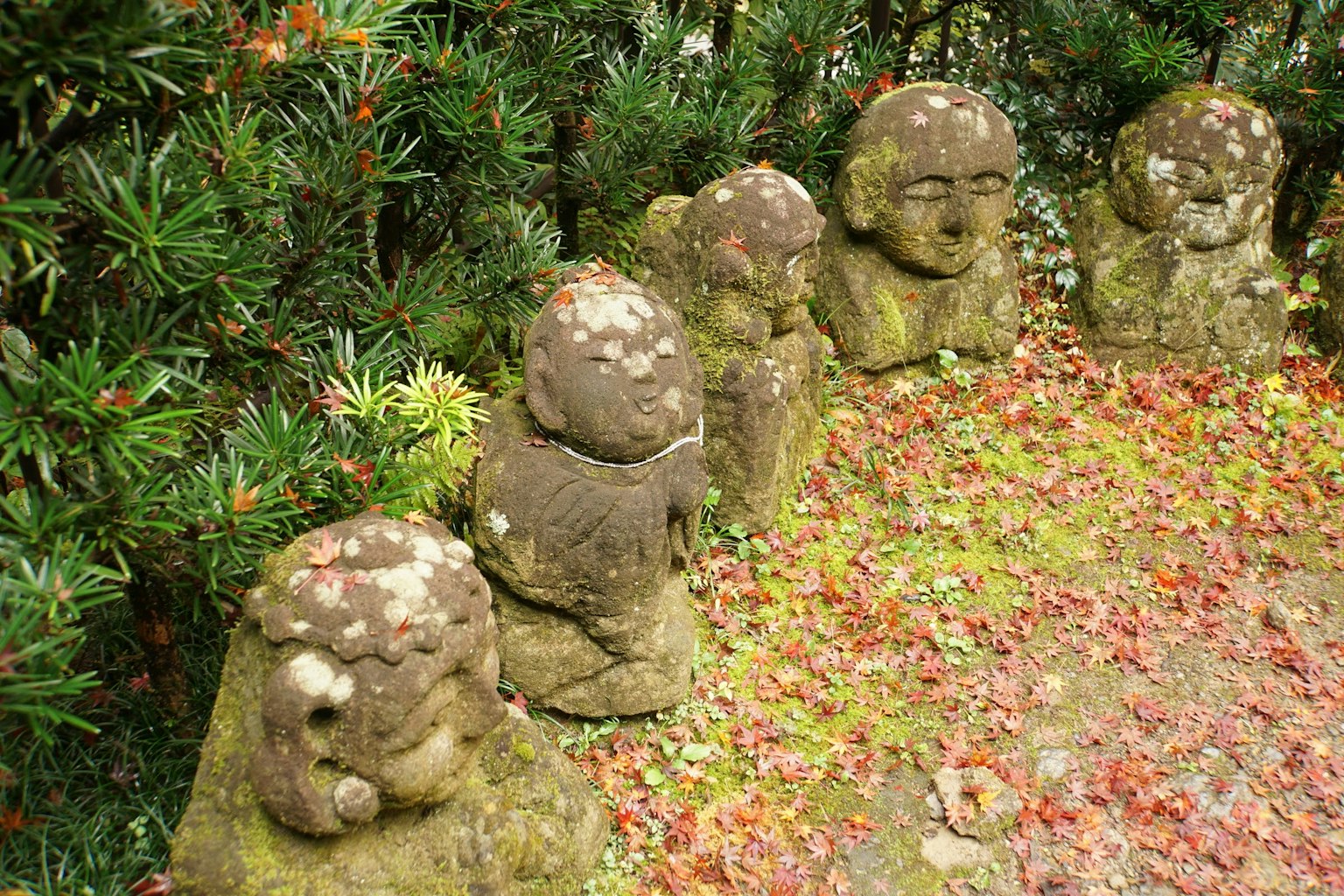 Una escena de jardín con pequeñas esculturas de piedra alineadas y hojas coloridas esparcidas
