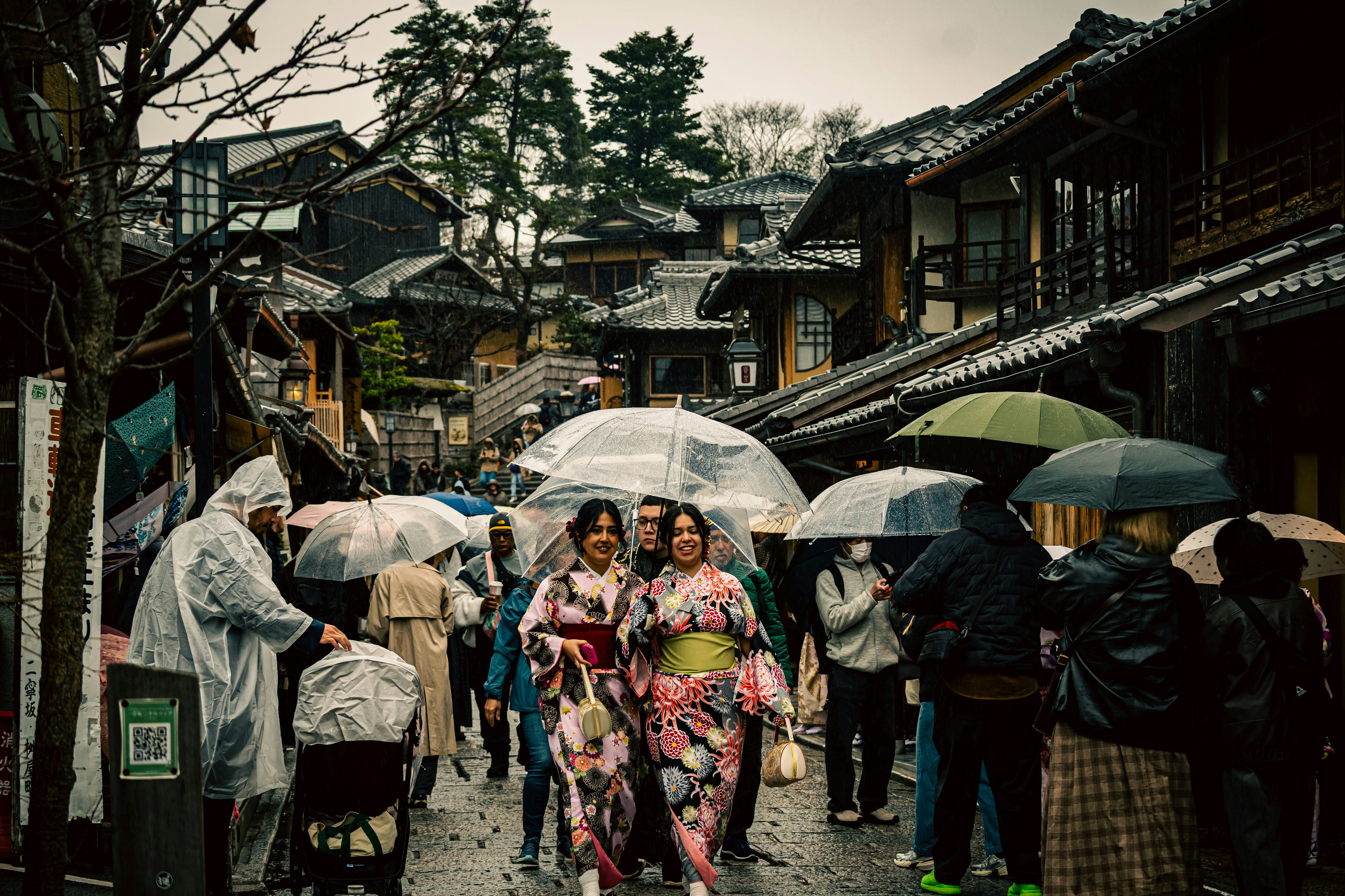 雨の路地で傘をさす人々が行き交う町並み