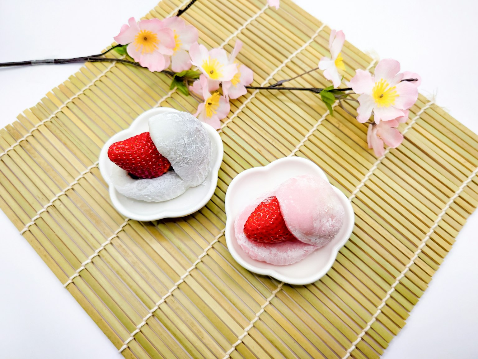 Dua daifuku stroberi berwarna putih dan merah muda di piring kecil dengan bunga sakura