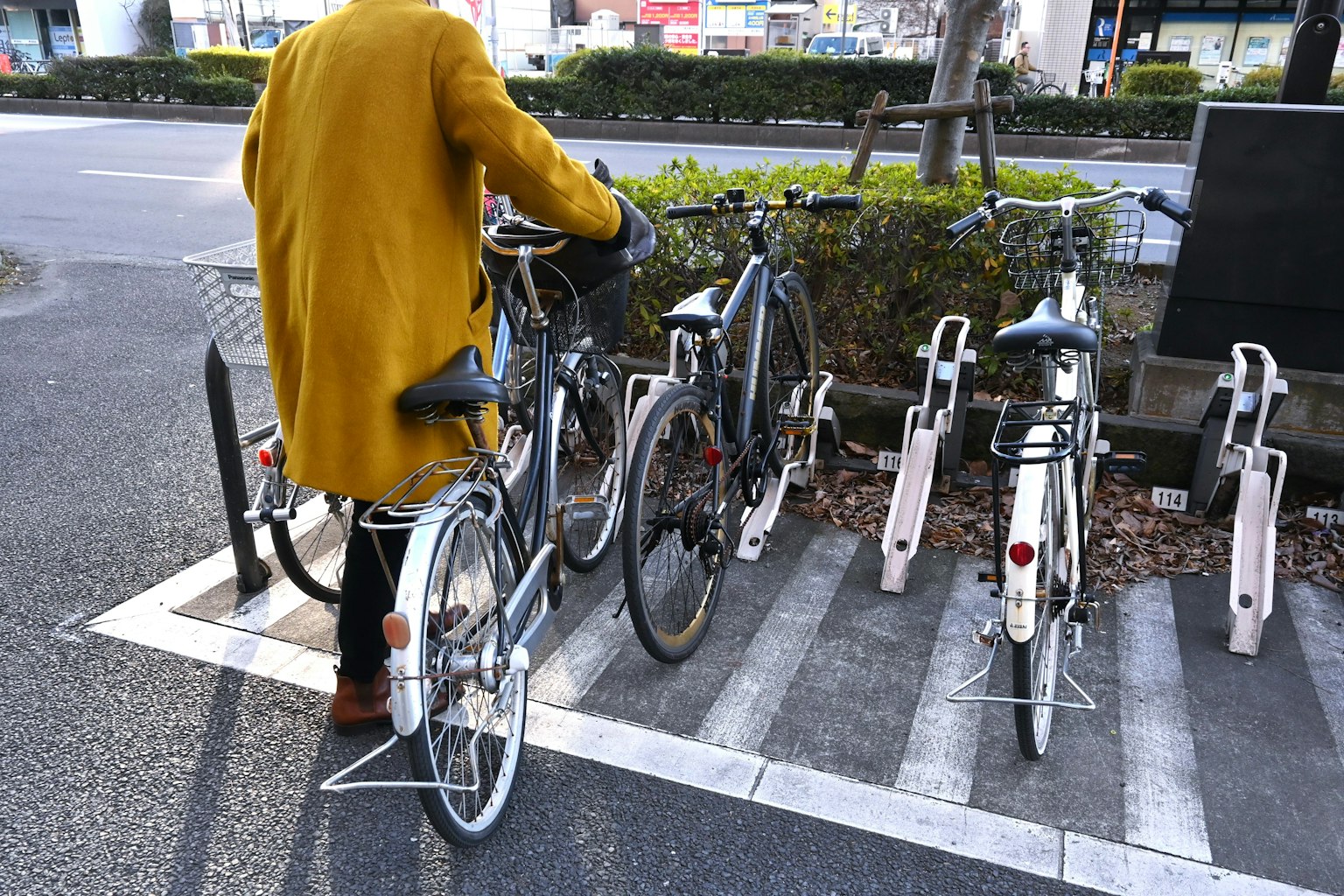 Persona estacionando una bicicleta en un aparcamiento para bicicletas con un abrigo amarillo