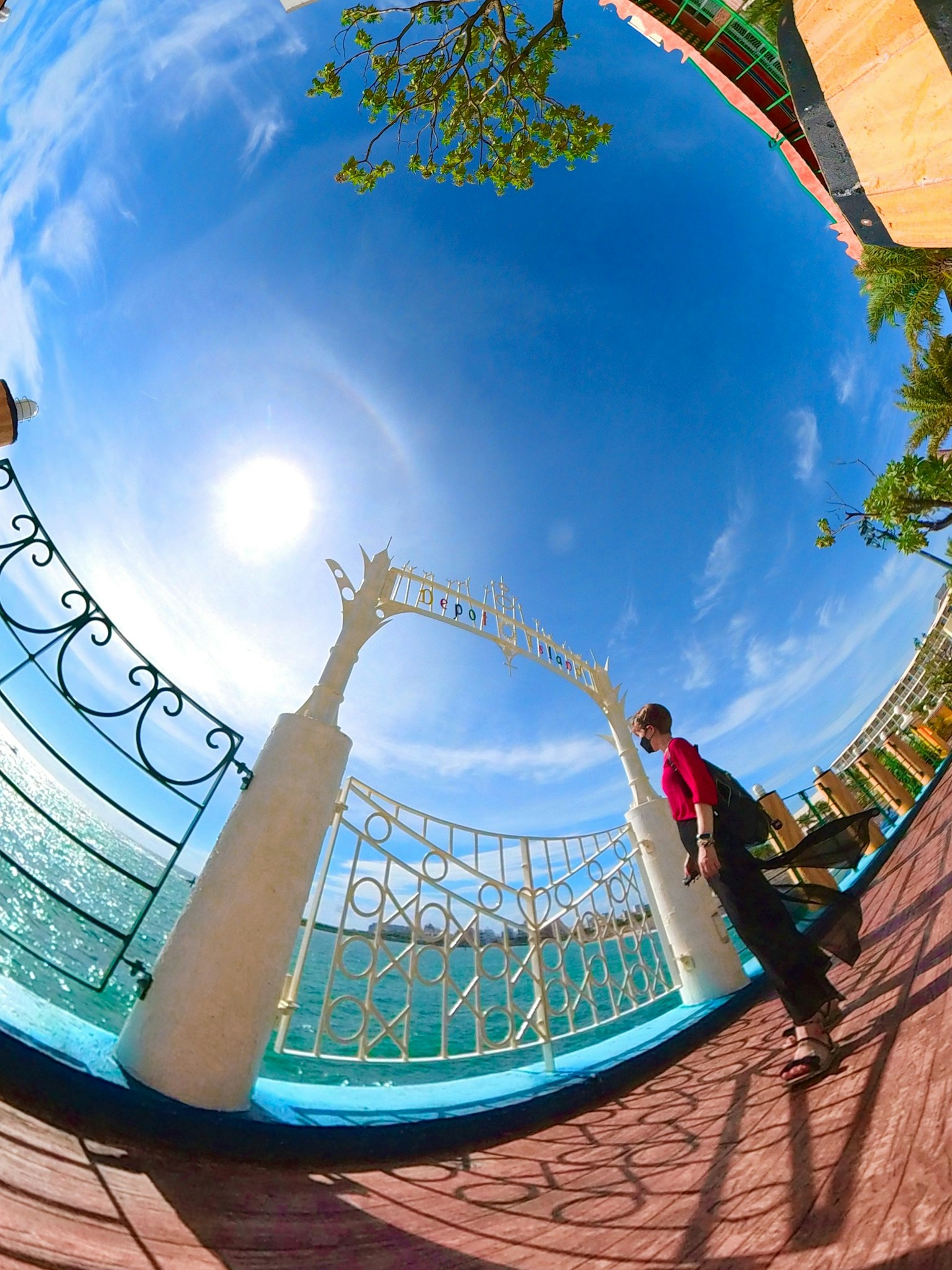 Uferpromenade mit einem weißen Bogen und einem Geländer unter einem strahlend blauen Himmel und Sonne